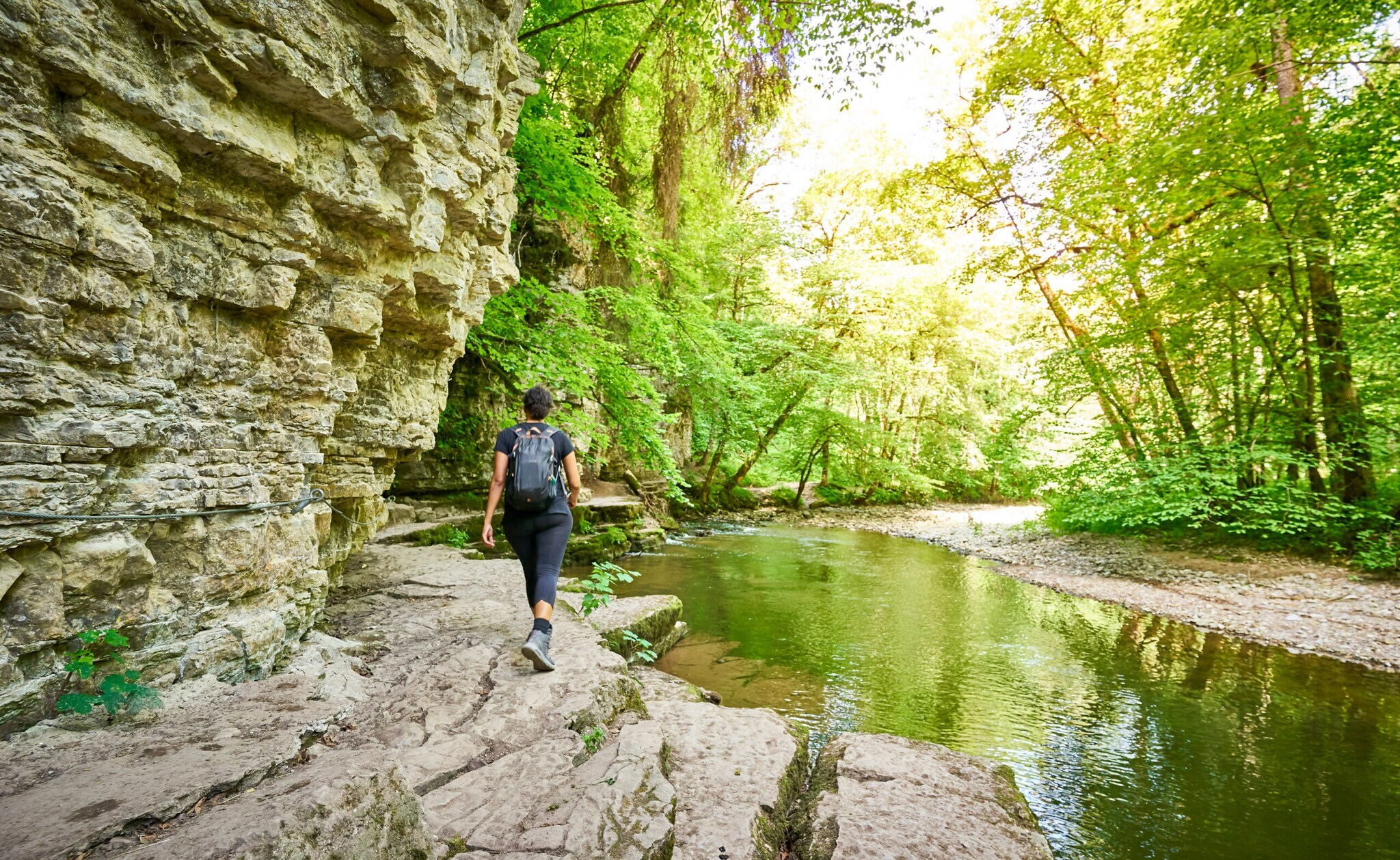 Eine Person mit Rucksack wandert an einem Fluss entlang Eine Person mit Rucksack wandert an einem Fluss entlang