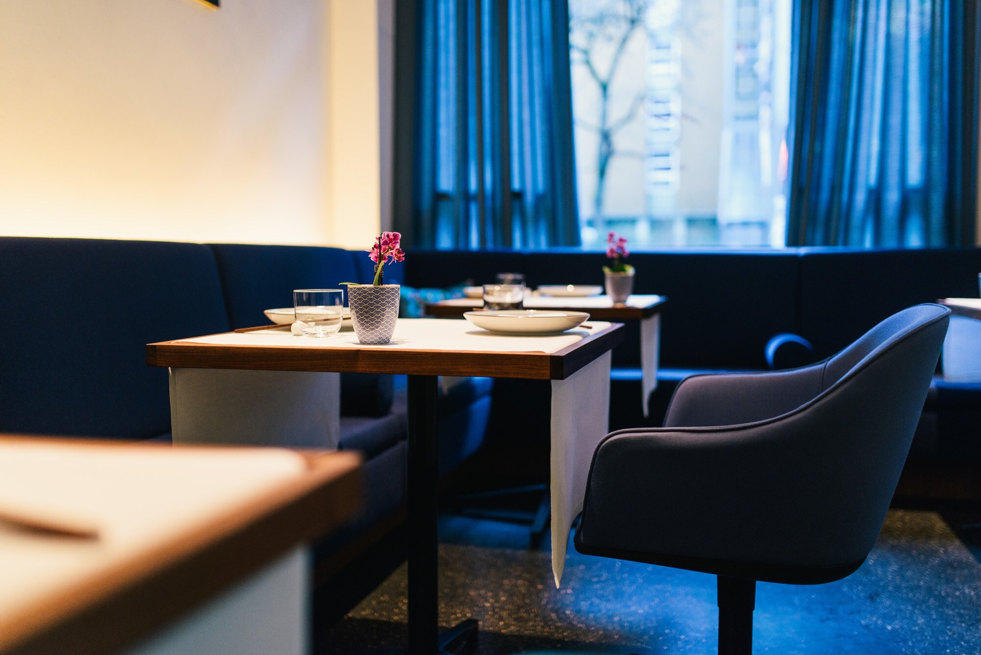 Drei eingedeckte, viereckige Holztische im Restaurant Tim Raue und blaue, gepolsterte Stühle