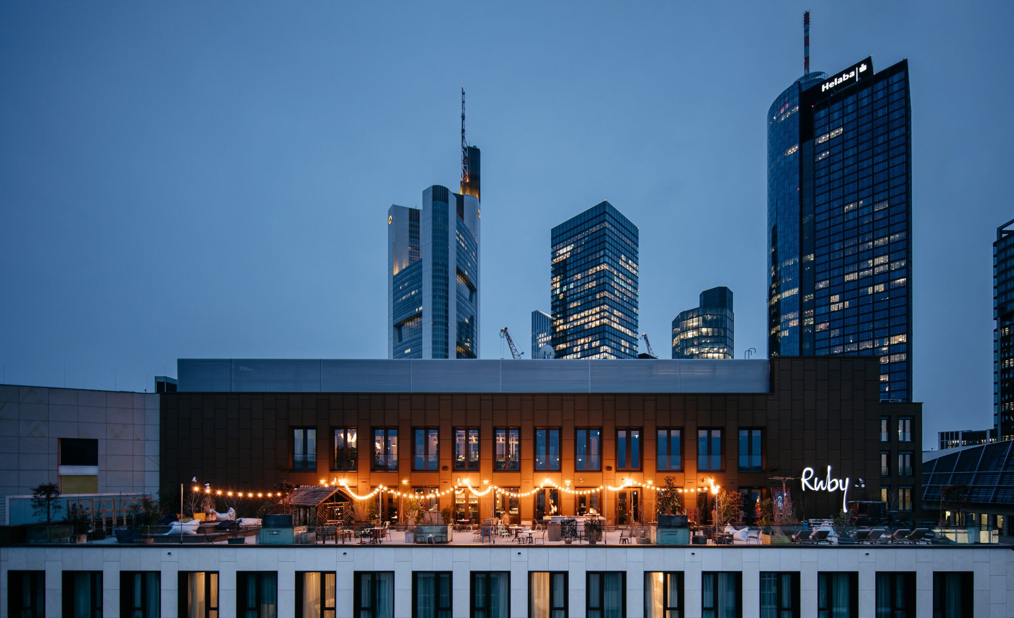 Eine beleuchtete Rooftop-Bar vor der Frankfurter Skyline bei Nacht