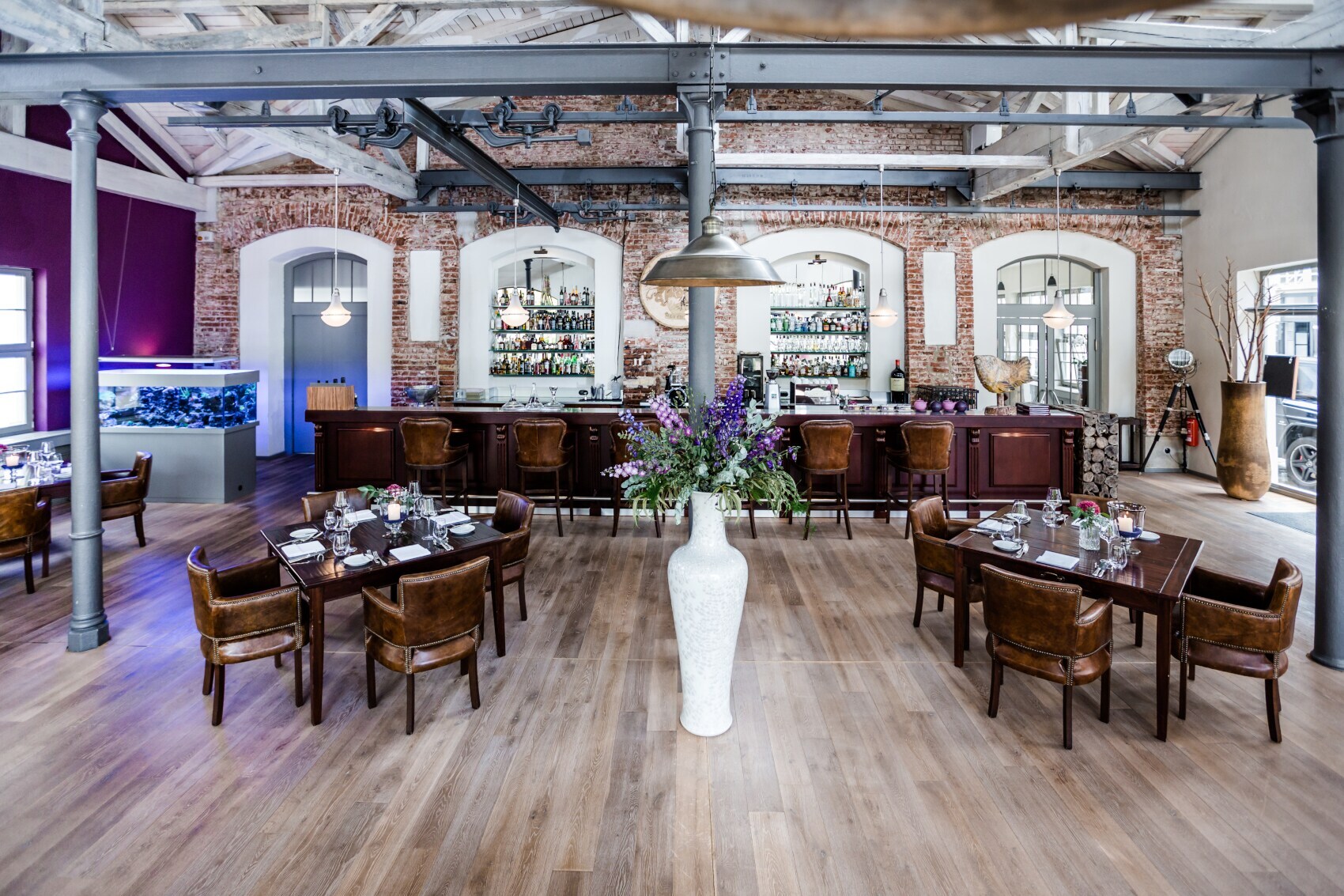 Mehrere eingedeckte Holztische im Restaurants Elements, im Vordergrund eine große weiße Vase mit Blumen, im ein dunkler Bartresen