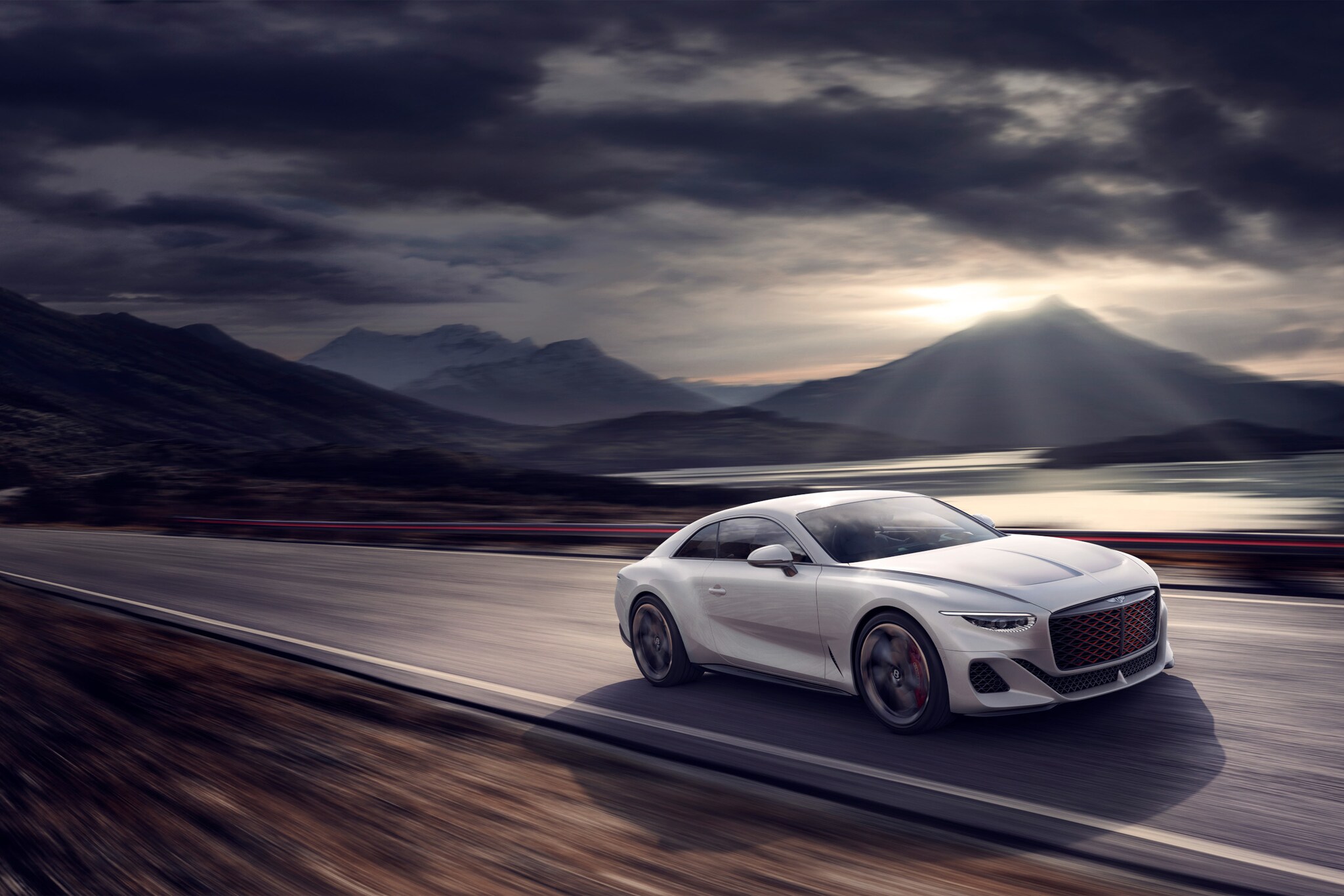 Weißes Auto von Bentley auf einer Straße, im Hintergrund Berge und Wolken