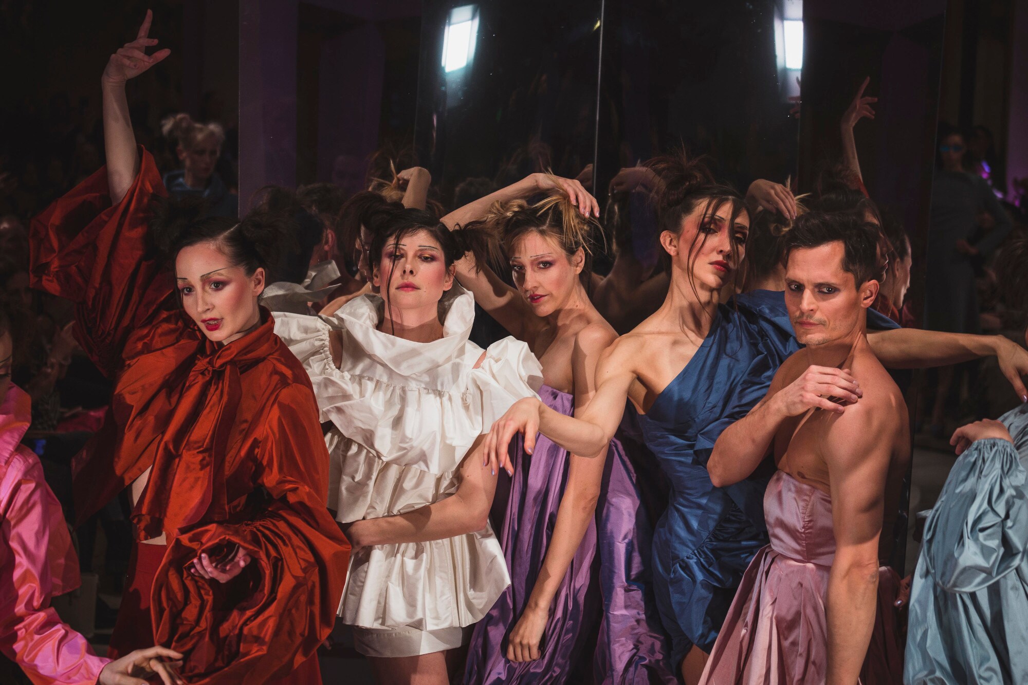 Weibliche und männliche Models posieren während einer Modenschau in glänzenden Kleidern Weibliche und männliche Models posieren während einer Modenschau in glänzenden Kleidern