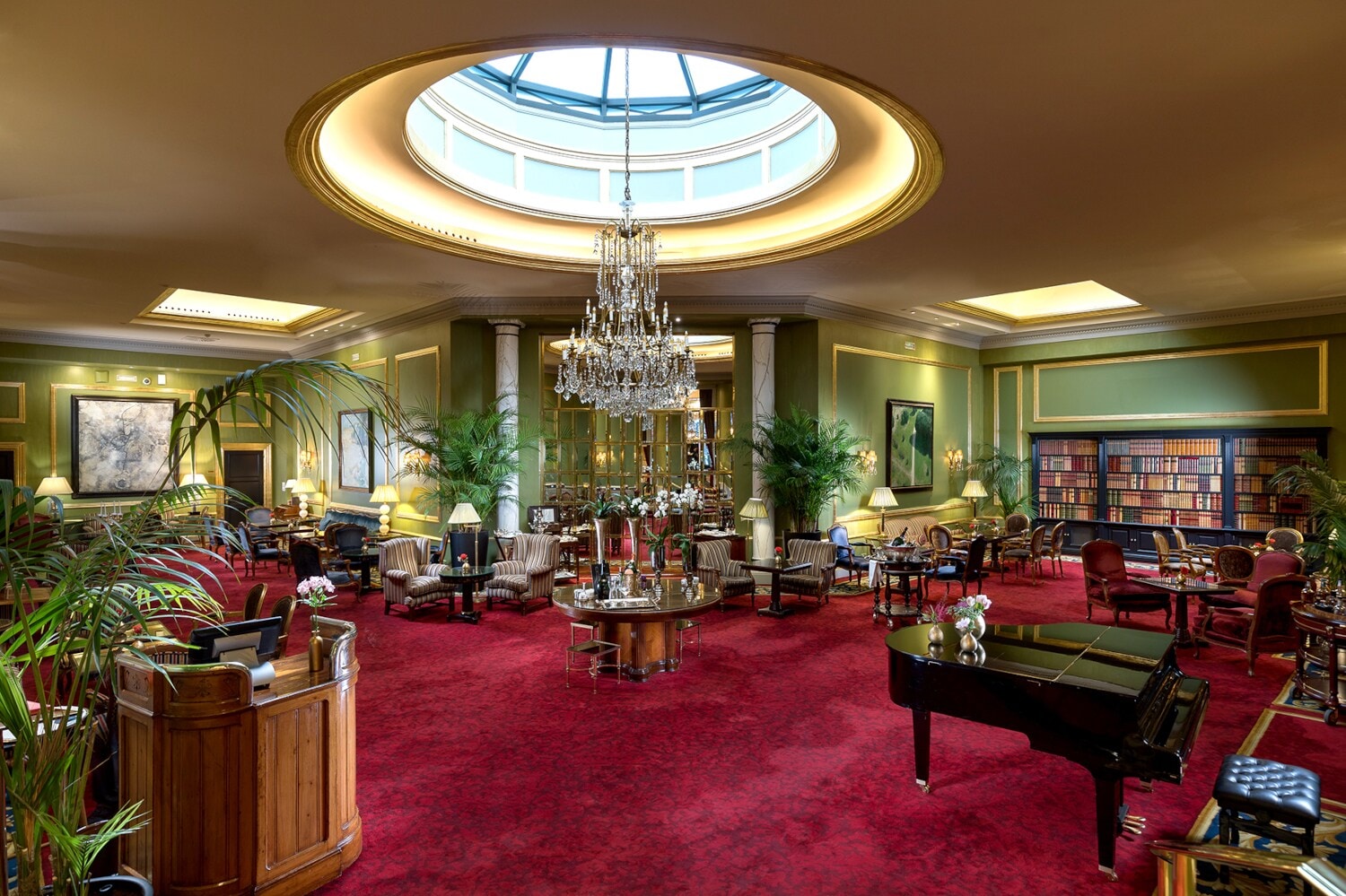 Elegante Hotellobby mit Kronleuchter und rotem Teppichboden, auf dem sich ein Piano und Sitzgelegenheiten befinden Elegante Hotellobby mit Kronleuchter und rotem Teppichboden, auf dem sich ein Piano und Sitzgelegenheiten befinden
