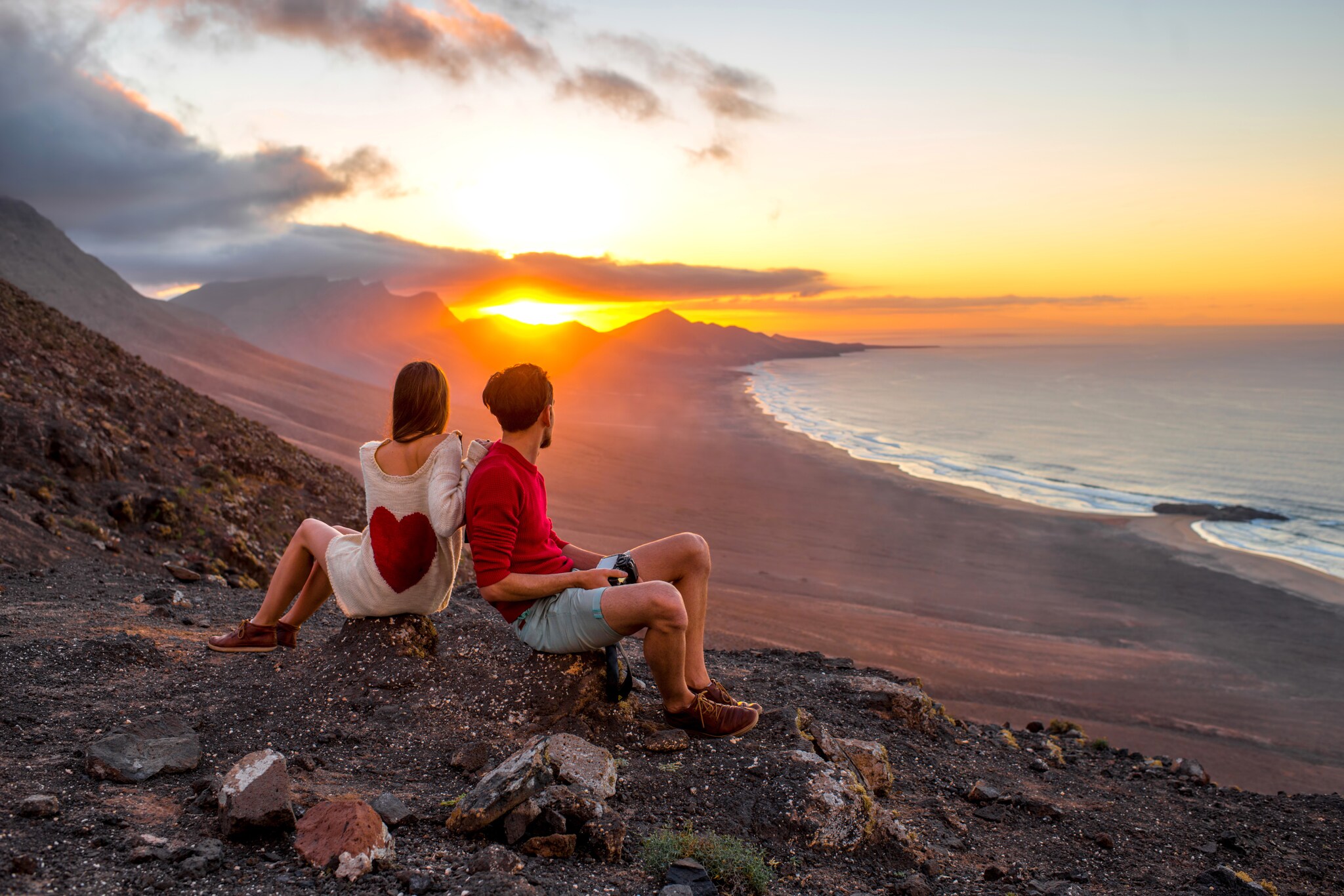 Zwei Menschen blicken bei ihrer Wanderung auf Fuerteventura aufs Meer bei Sonnenuntergang
