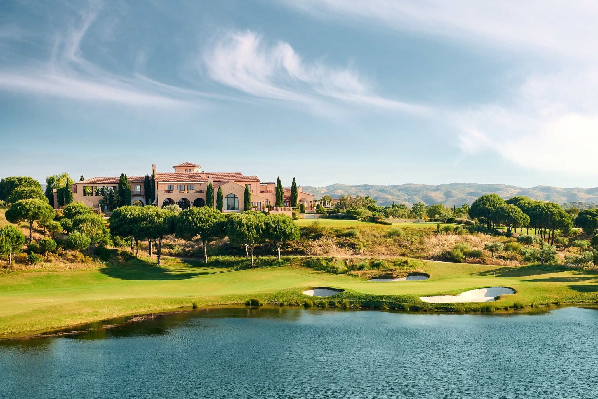Ein Klubhaus auf einem Golfplatz mit Bäumen und einem See Ein Klubhaus auf einem Golfplatz mit Bäumen und einem See
