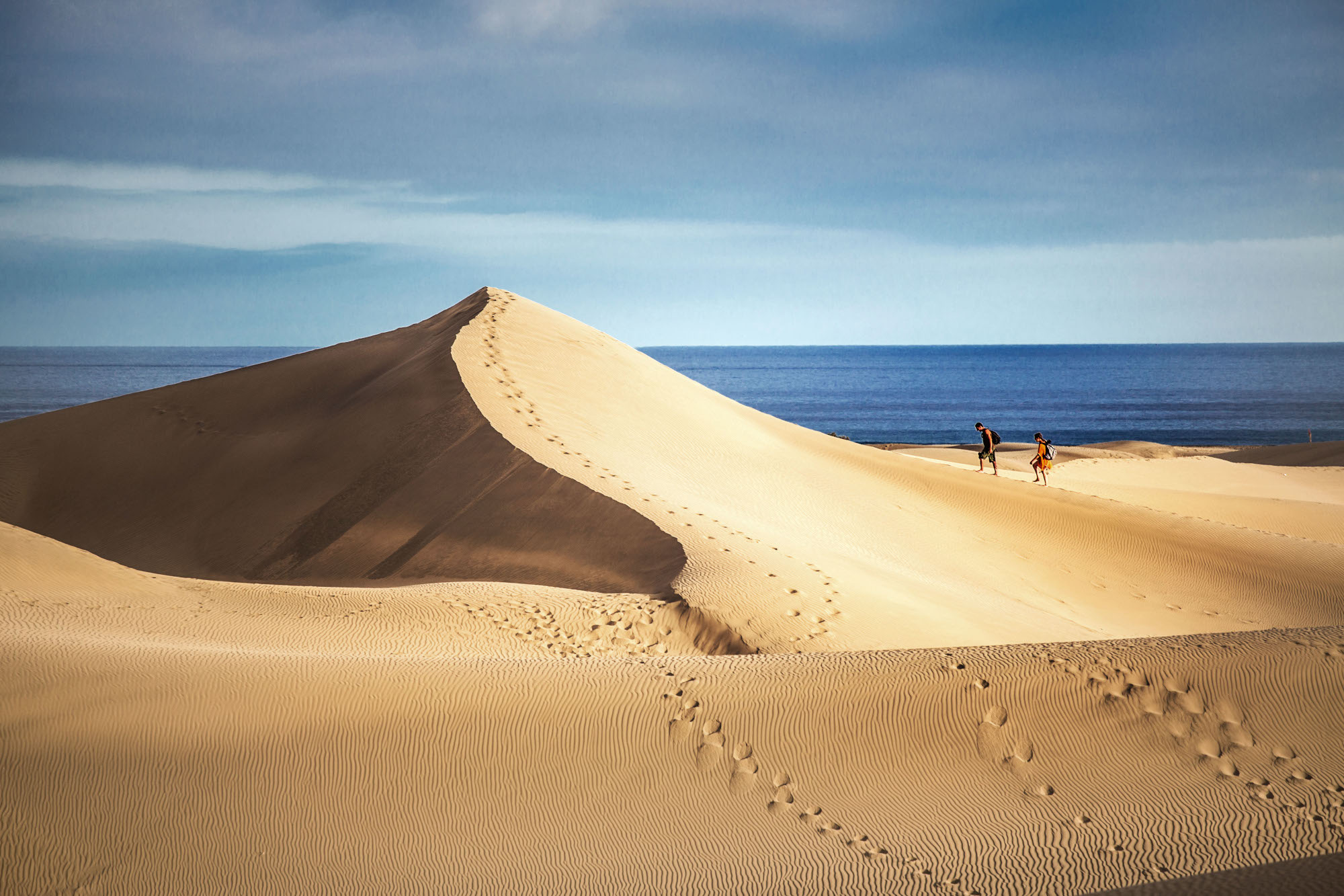 Zwei Personen wandern auf einer großen Sanddüne am Meer