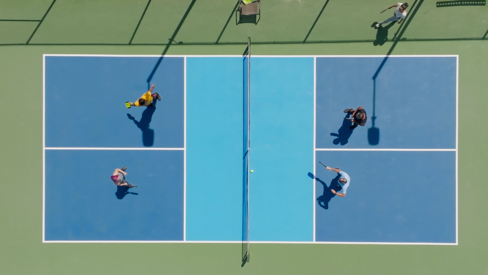 Top-Down-Aufnahme von vier Personen auf einem Tennisplatz, die Pickleball als Doppel spielen