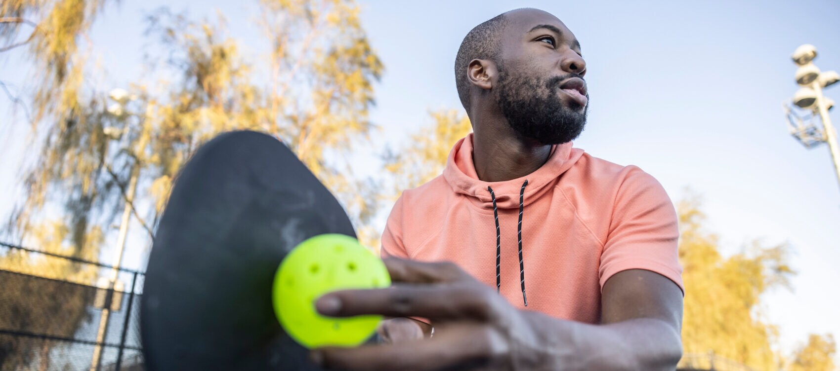 Nahaufnahme eines Spielers beim Aufschlag beim Pickleball auf einem Sportplatz unter freiem Himmel