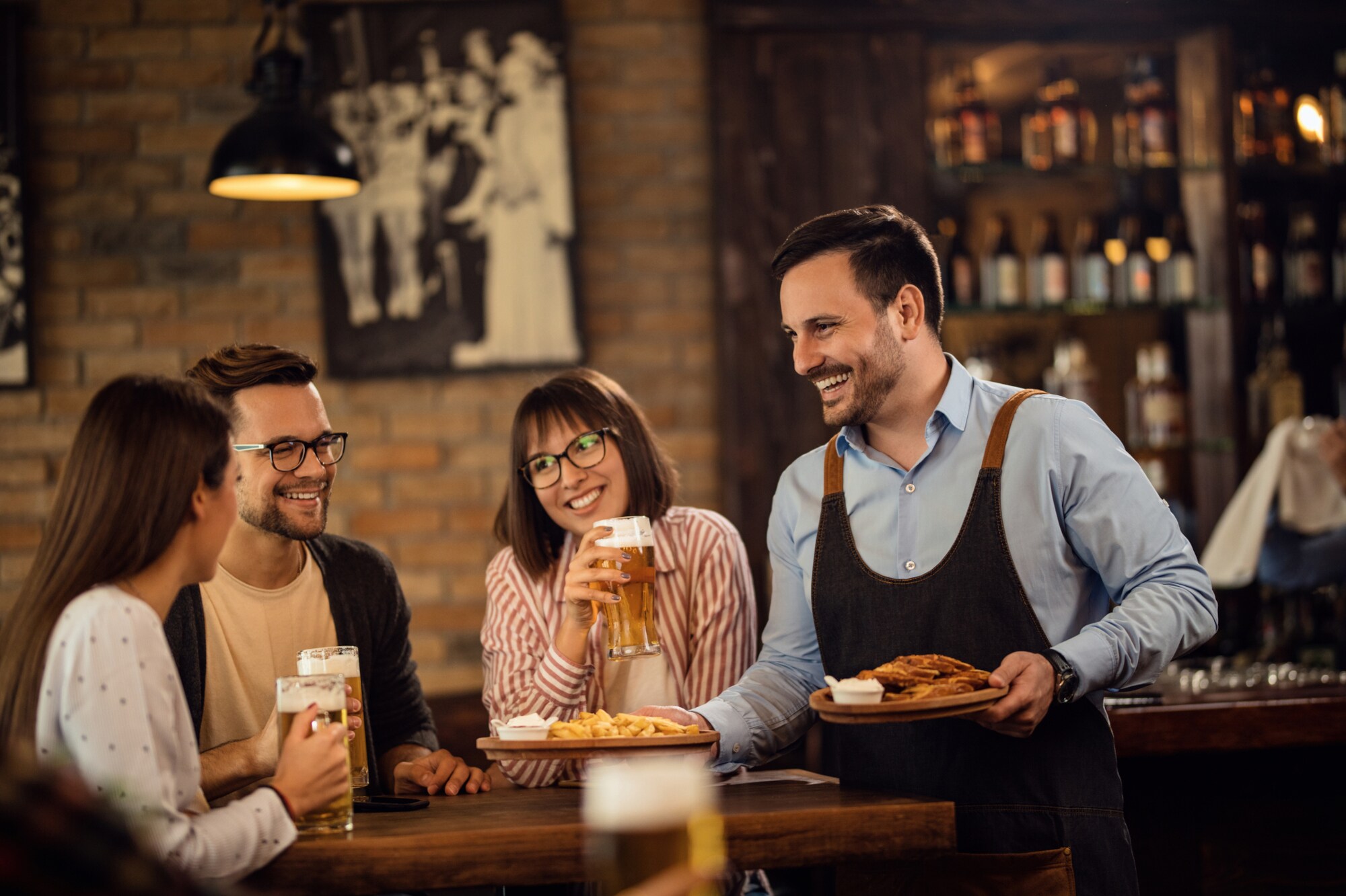 Lächelnder Kellner, der einer Gruppe von Gästen in einem Pub Essen bringt
