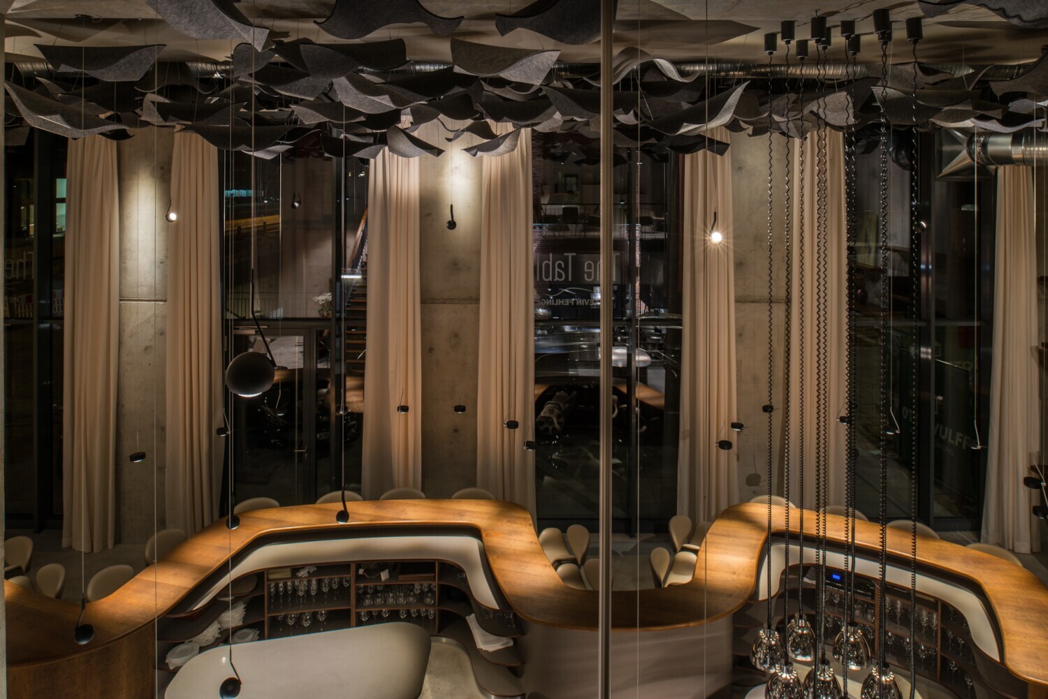 Blick auf das leere Restaurant The Table mit dem geschwungenen Holztisch und hohen Fenstern im Hintergrund Blick auf das leere Restaurant The Table mit dem geschwungenen Holztisch und hohen Fenstern im Hintergrund