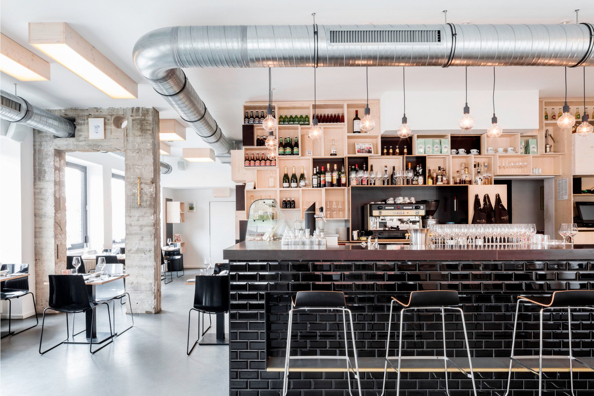 Der im Industrial Stil gestaltete Innenraum des maiBeck mit schwarzem Tresen und Chromstühlen.