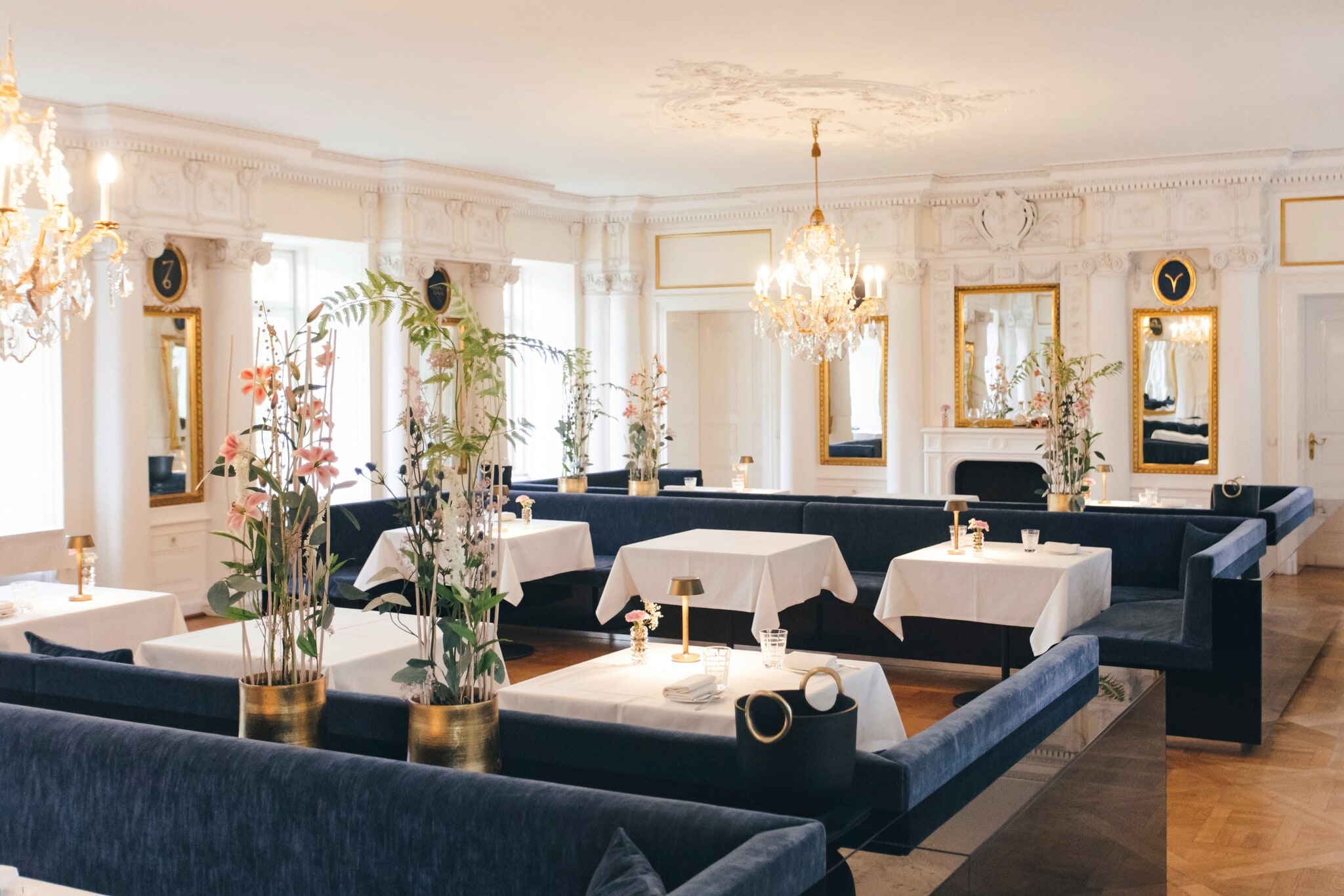 Innenaufnahme eines edlen Restaurants mit Kronleuchtern und gedeckten Tischen an blauen Samtbänken Innenaufnahme eines edlen Restaurants mit Kronleuchtern und gedeckten Tischen an blauen Samtbänken