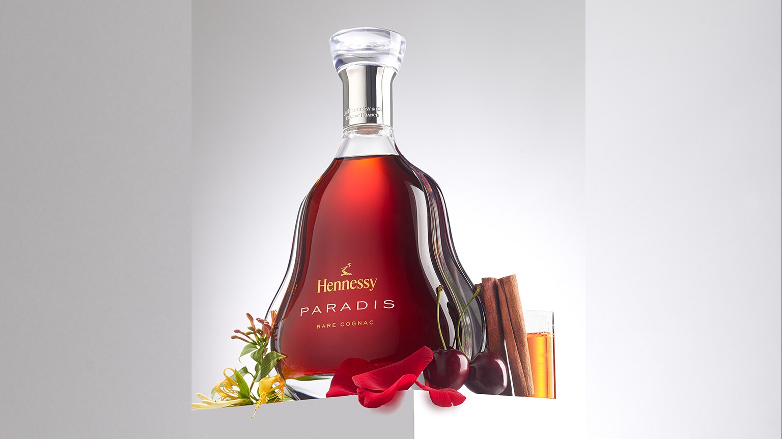 Eine Flasche Hennessy Paradise umgeben von Kirschen, Blütenblättern und Zimtstangen