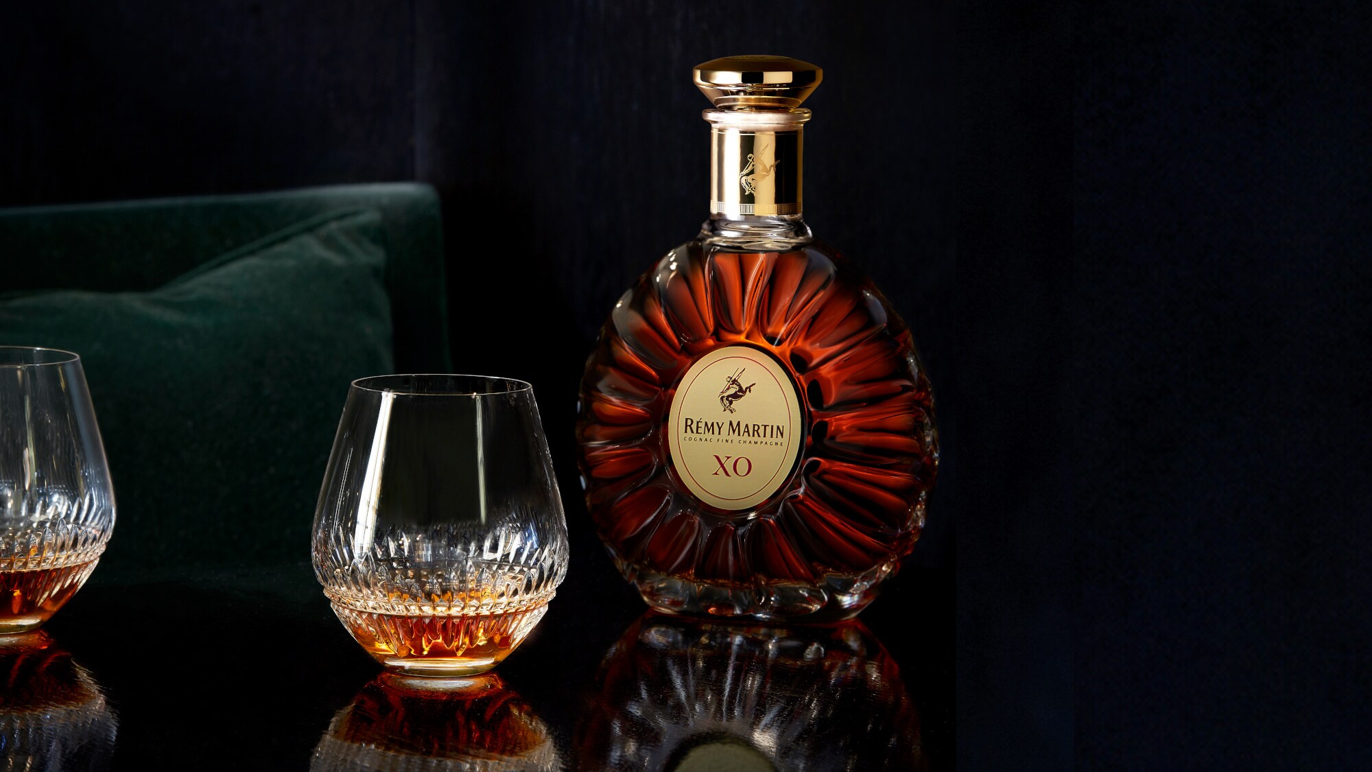 Eine Flasche Rémy Martin XO vor schwarzen Hintergrund, daneben ein gefülltes Cognac-Glas