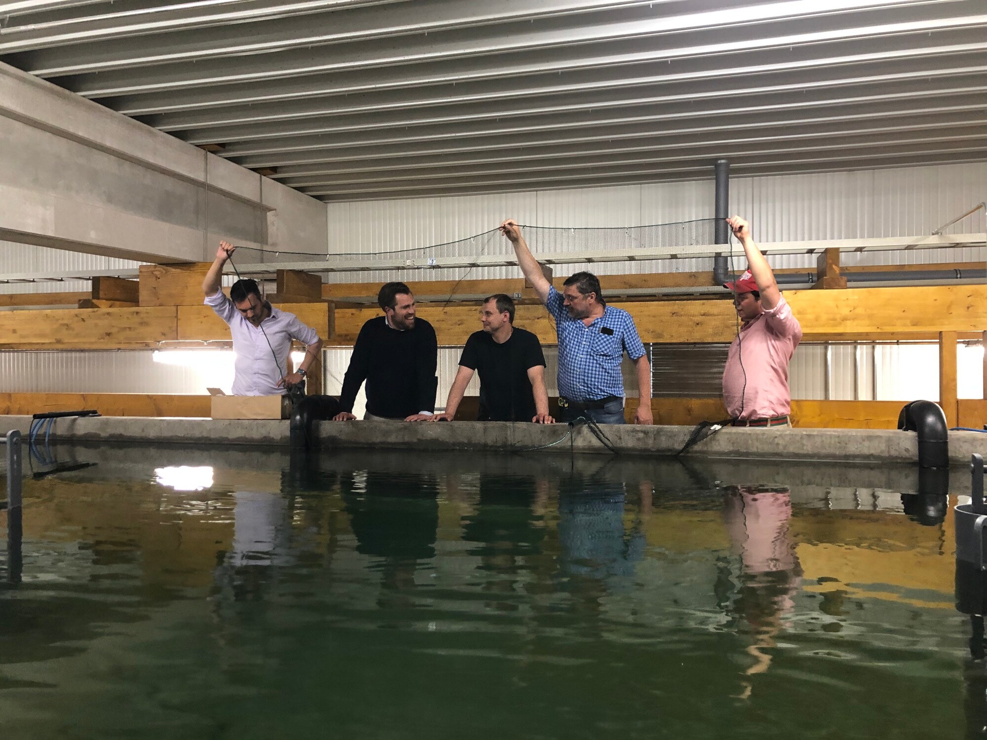 Fünf Männer stehen an einem Becken, drei von ihnen halten ein Netz in die Höhe
