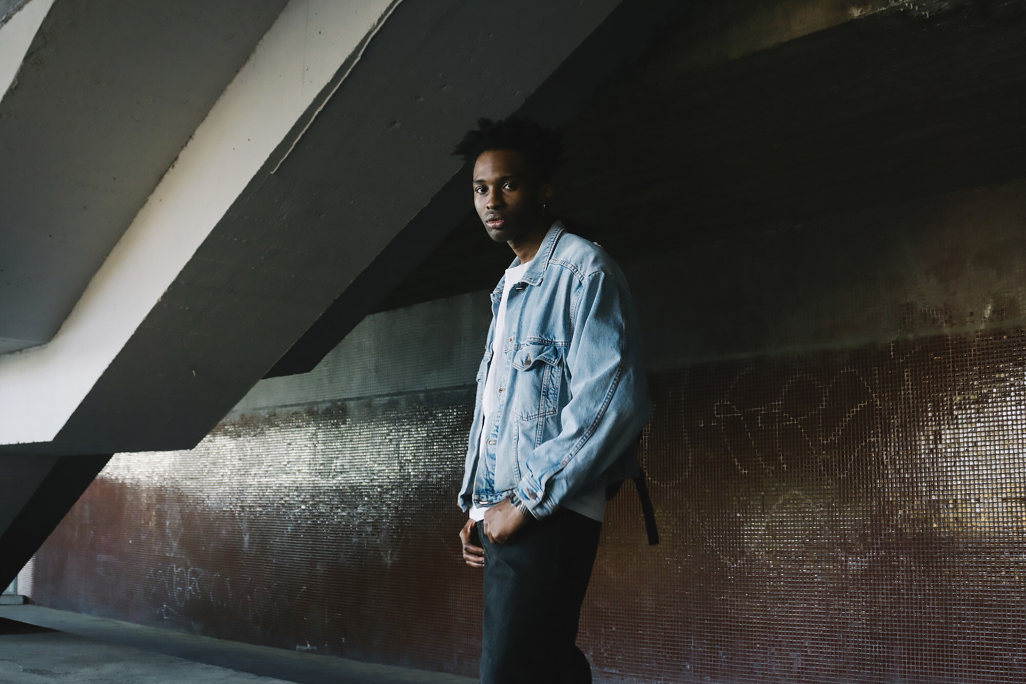 Ein stylischer junger Mann posiert in Jeansjacke in urbaner Umgebung