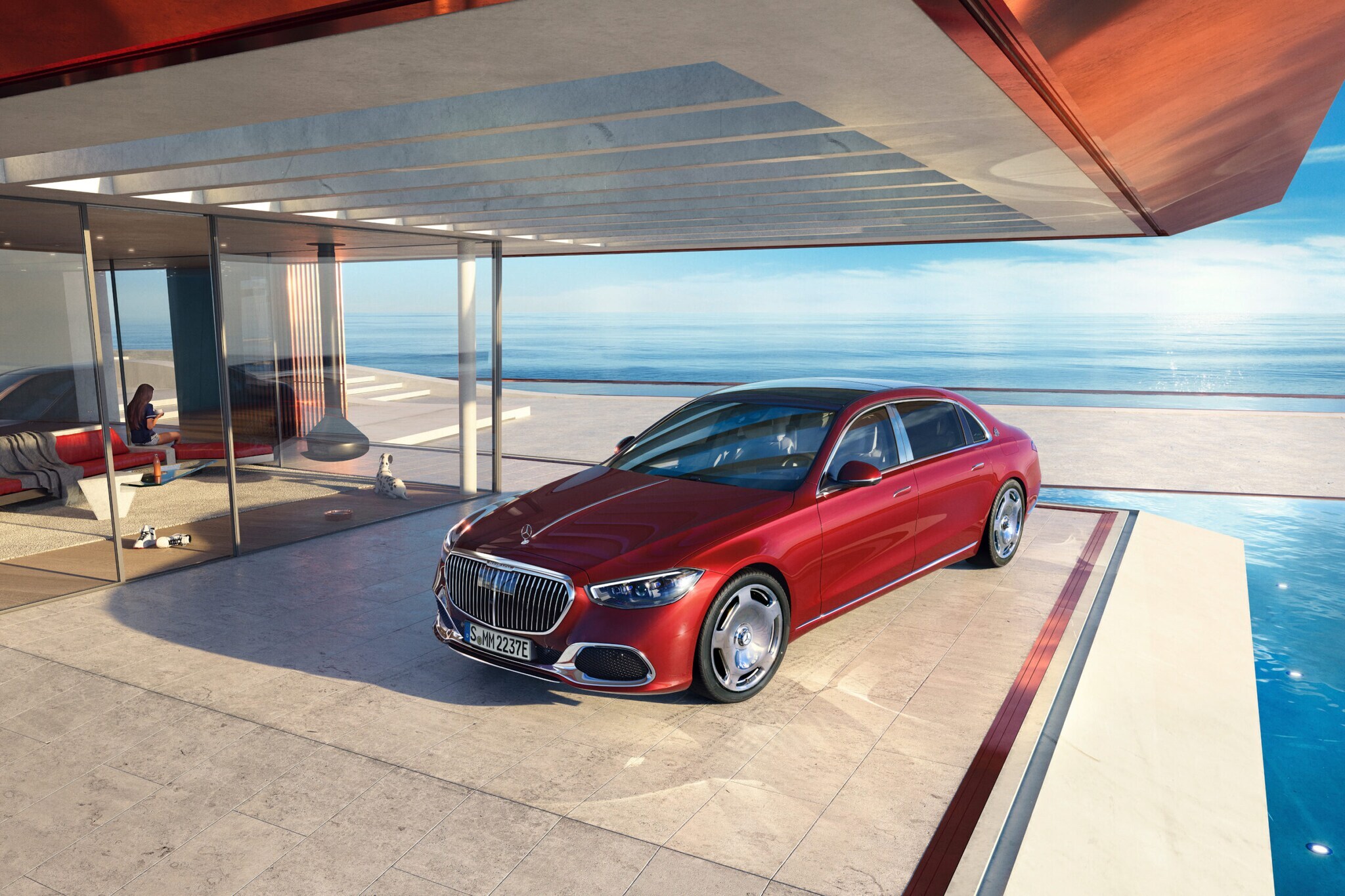 Ein roter Mercedes-Maybach seitlich von vorne am Pool auf der Terrasse eines modernen Hauses mit viel Glas, im Hintergrund blaues Meer