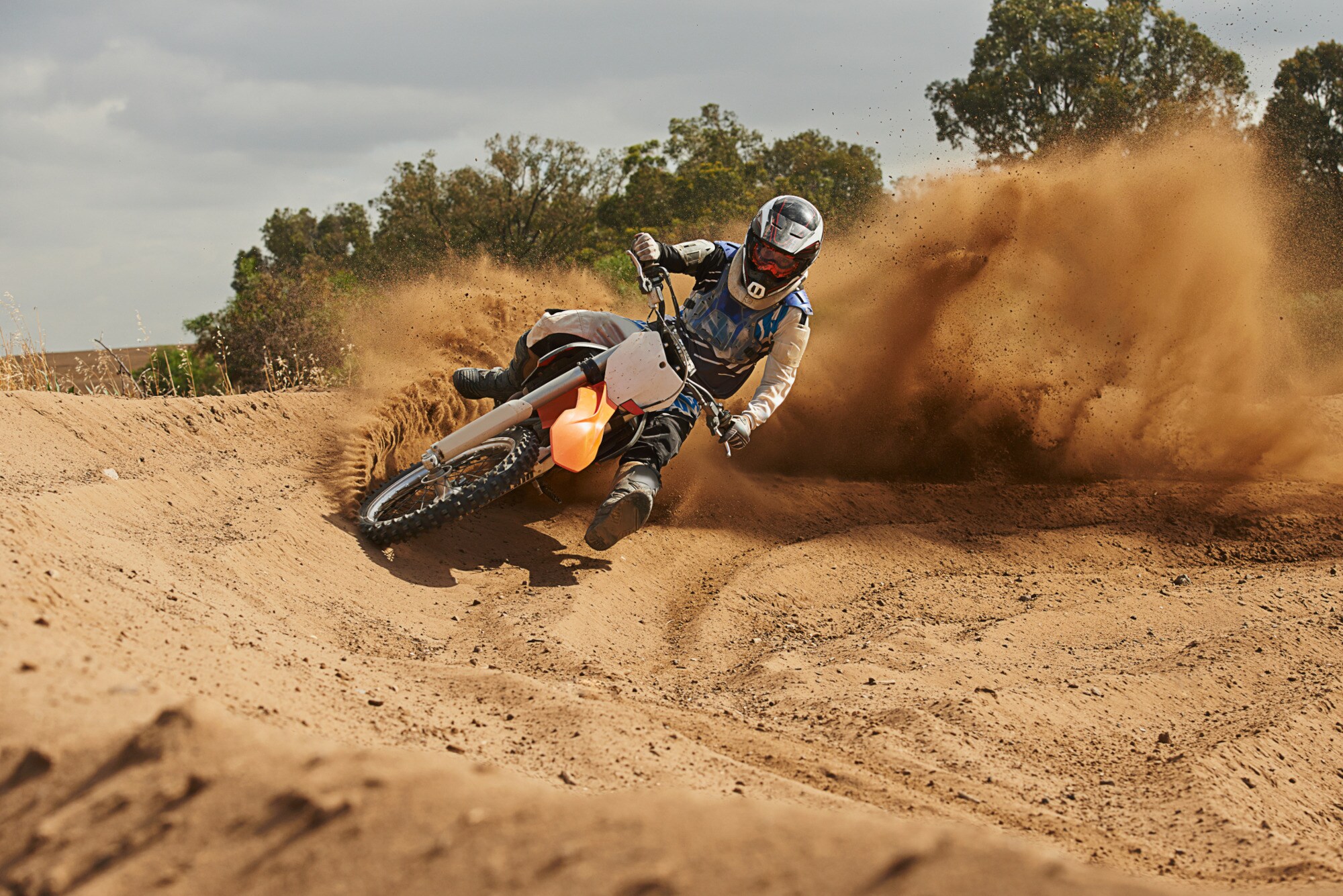 Eine Person fährt auf einem Motocrossbike um die Kurve und wirbelt Sand auf Eine Person fährt auf einem Motocrossbike um die Kurve und wirbelt Sand auf
