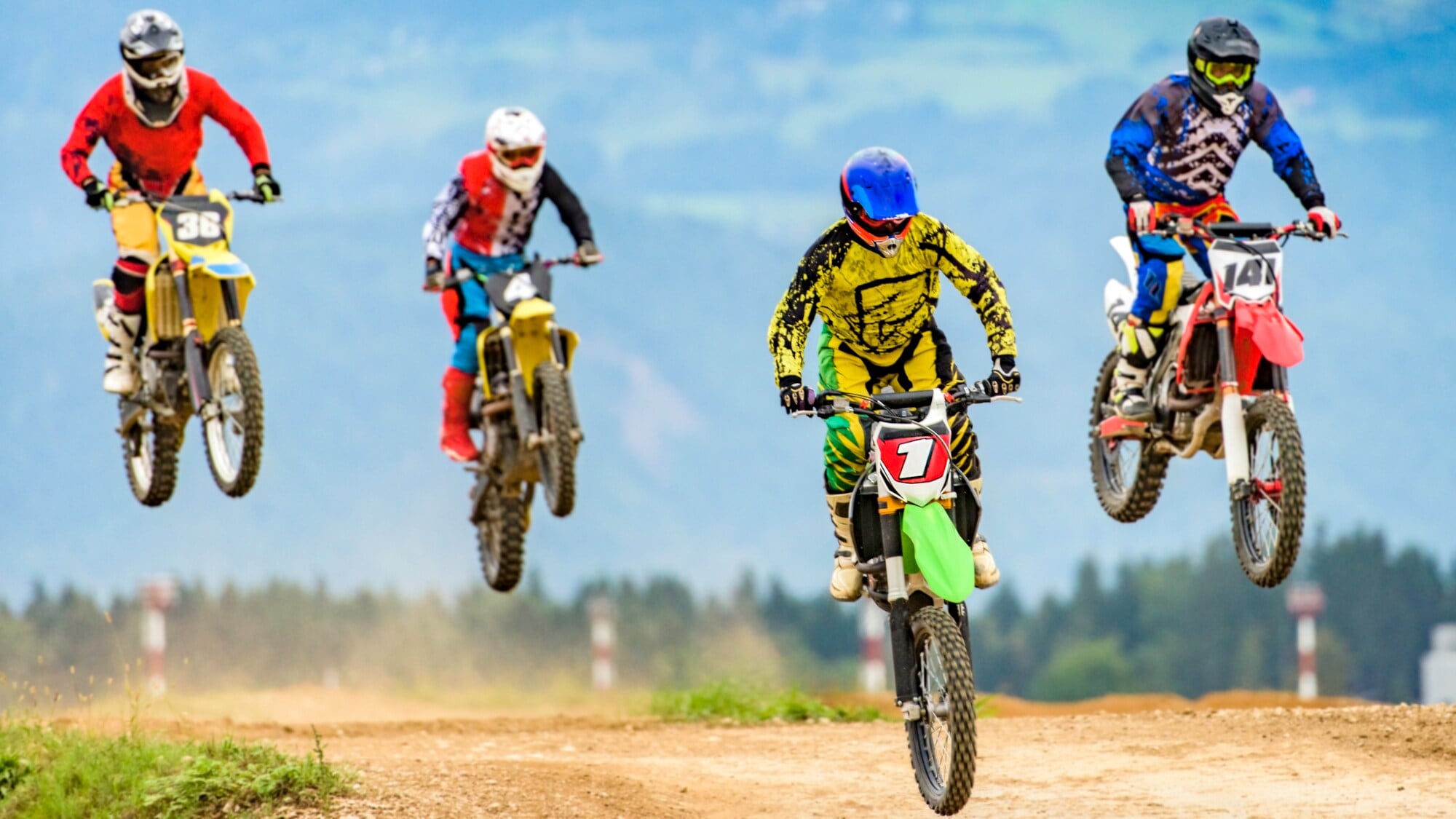 Vier Fahrer springen mit ihren Motocrossmotorrädern über eine Rennpiste Vier Fahrer springen mit ihren Motocrossmotorrädern über eine Rennpiste