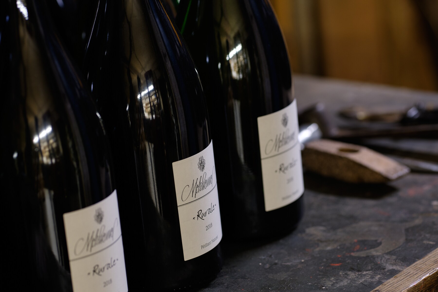 Drei Flaschen Pet Nat Rurale Riesling vom Mosel Weingut Melsheimer im Anschnitt auf einem Tisch