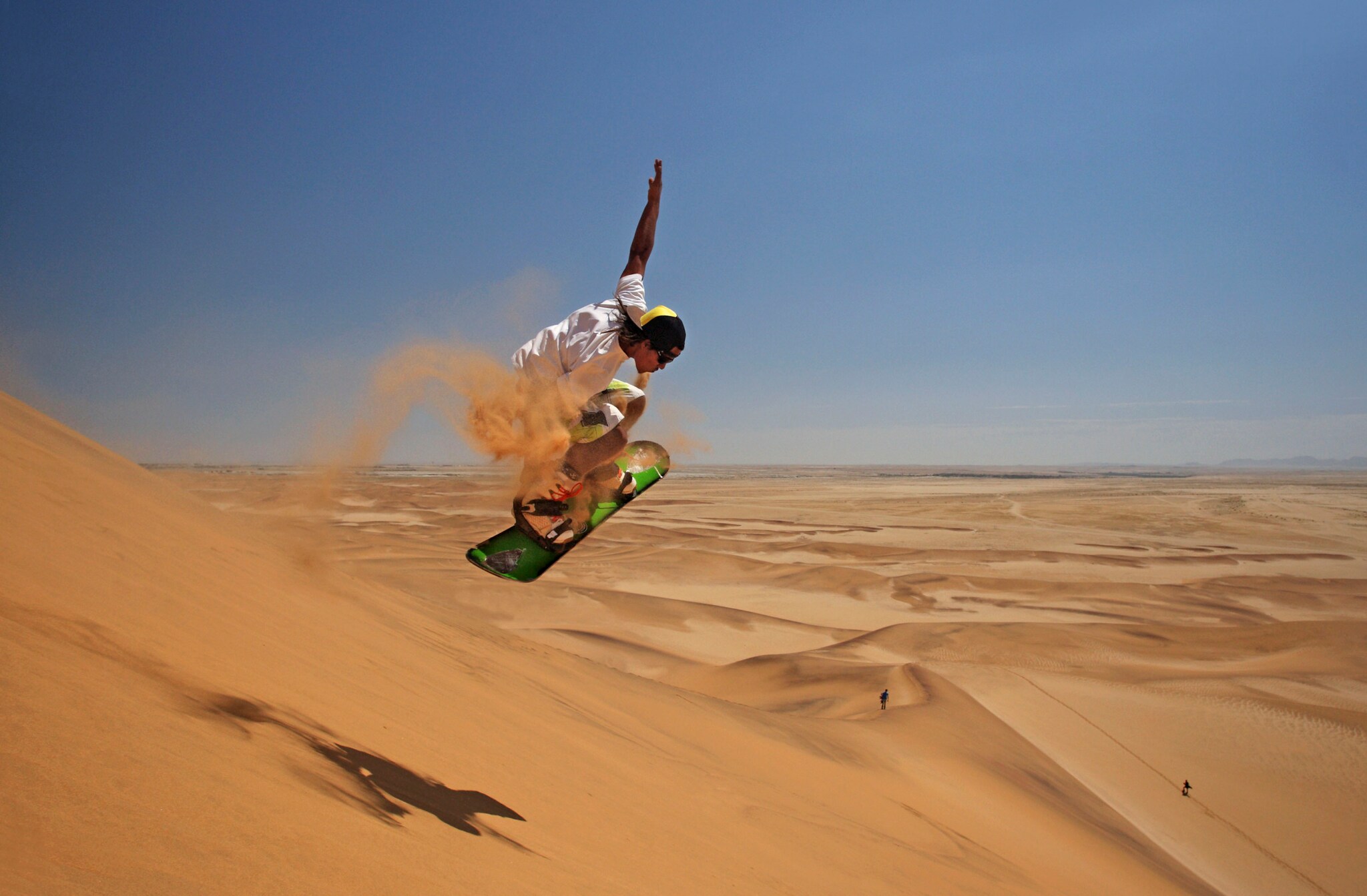 Ein Sandboarder beim Sprung auf einer Sanddüne in einer weiten Wüstenlandschaft Ein Sandboarder beim Sprung auf einer Sanddüne in einer weiten Wüstenlandschaft