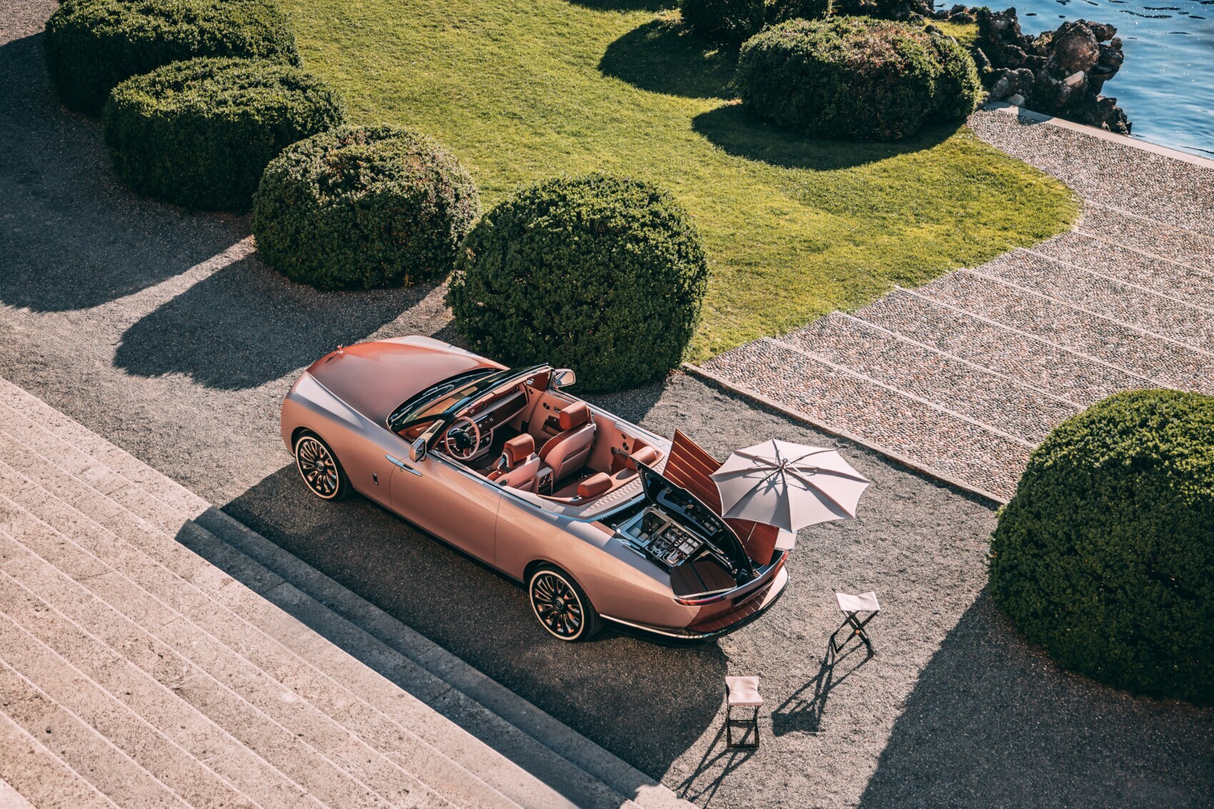 Luftaufnahme des Rolls-Royce Boat Tail in Roségold, das in einer prächtigen Parkanlage steht und einen Blick auf den Champagnerkühler gewährt