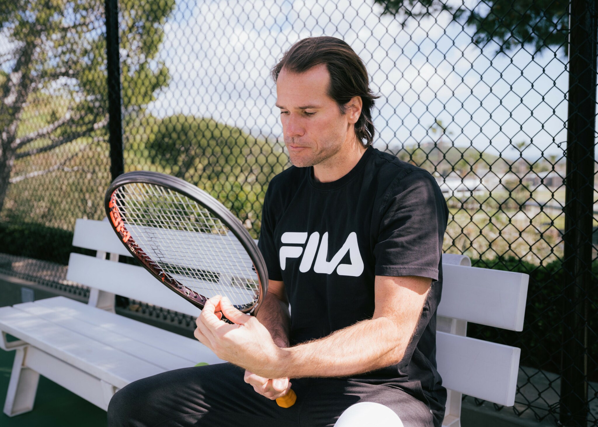 Tommy Haas sitzt auf einer Bank und zupft an den Saiten seines Tennisschlägers.