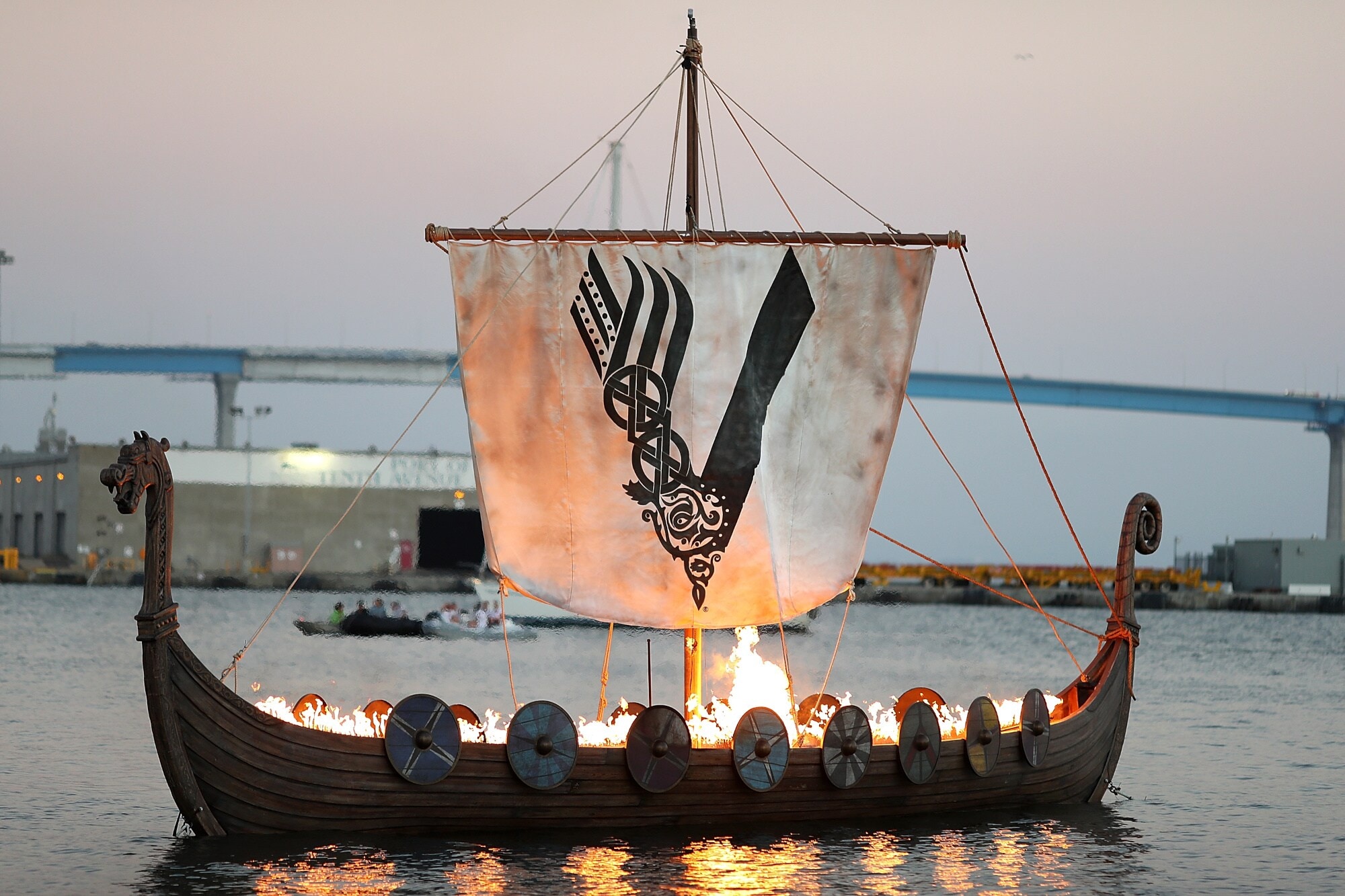 Aufnahme eines brennenden Wikingerschiffs auf dem Meer mit einem Segel, das das Logo der „Vikings“-Serie zeigt Aufnahme eines brennenden Wikingerschiffs auf dem Meer mit einem Segel, das das Logo der „Vikings“-Serie zeigt