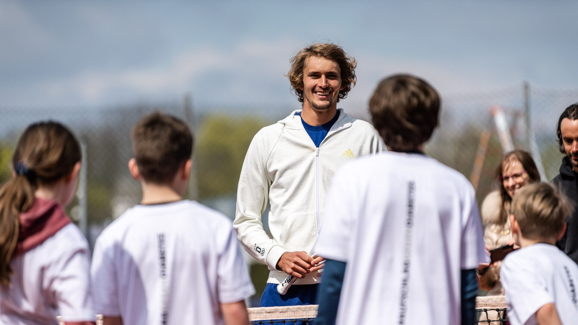 Alexander Zverev spricht zu Kindern auf einem Tennisplatz.