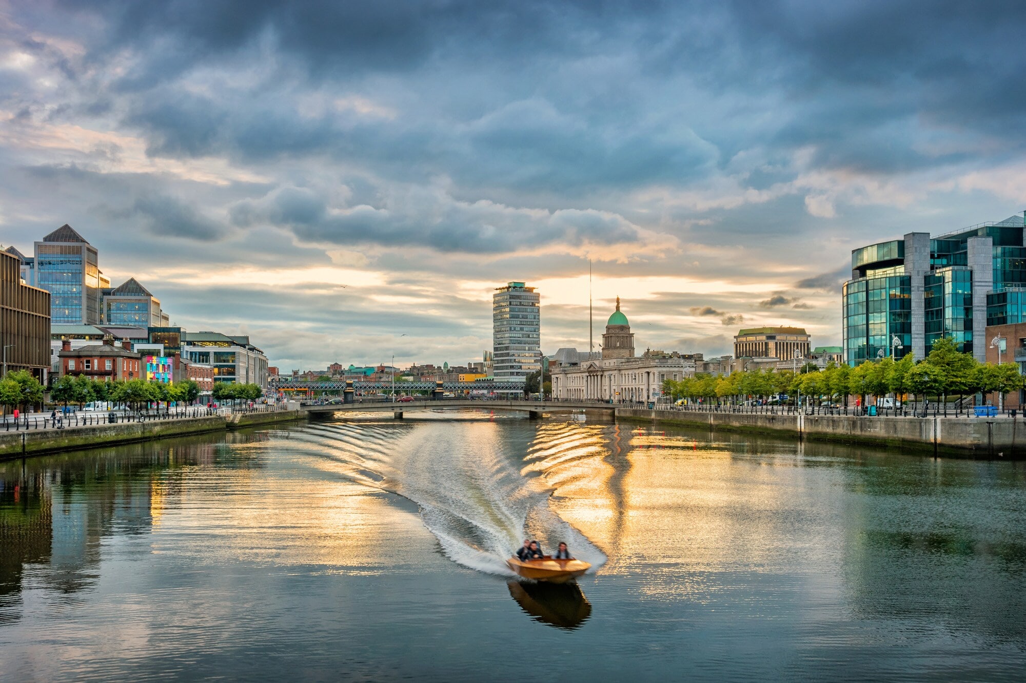 Ein Motorboot fährt auf dem Liffey River in Dublin bei Sonnenuntergang Ein Motorboot fährt auf dem Liffey River in Dublin bei Sonnenuntergang