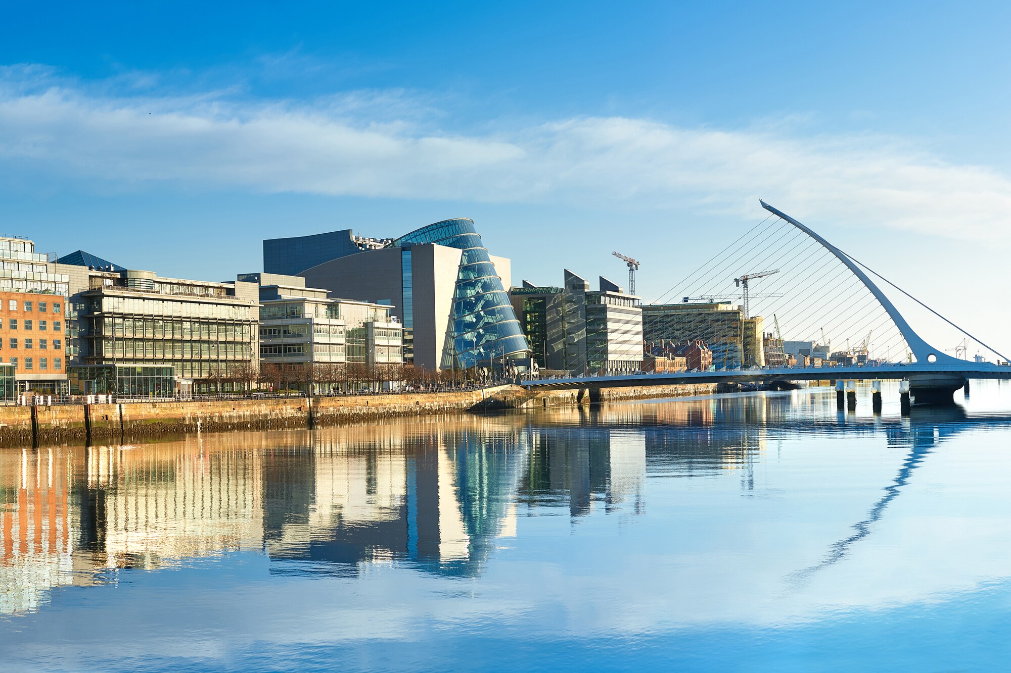 Moderne Gebäude sowie die Harfenbrücke über den Liffey River in Dublin an einem hellen, sonnigen Tag
