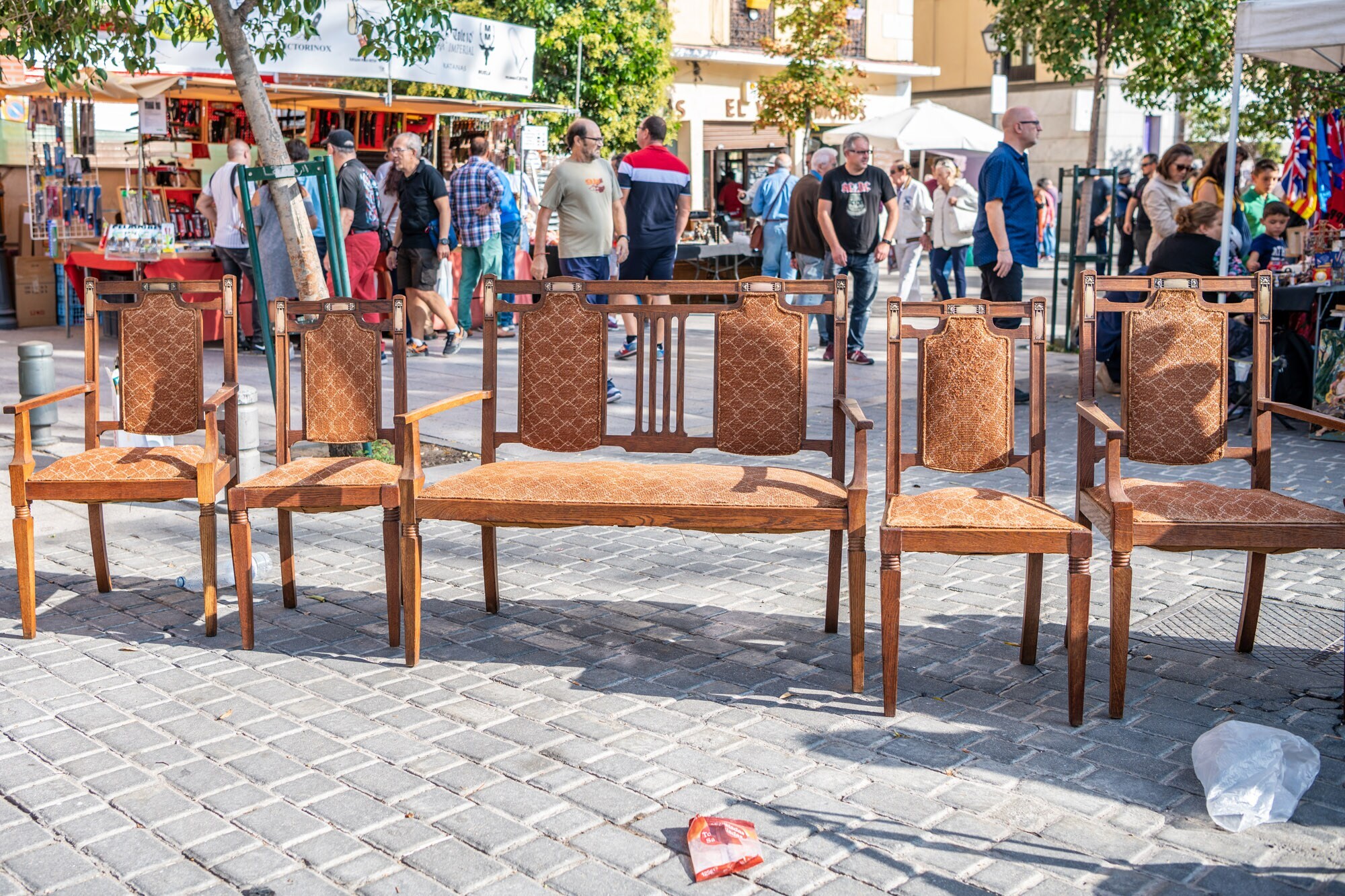 Mehrere gepolsterte Stühle stehen nebeneinander in einer belebten Fußgängerzone.
