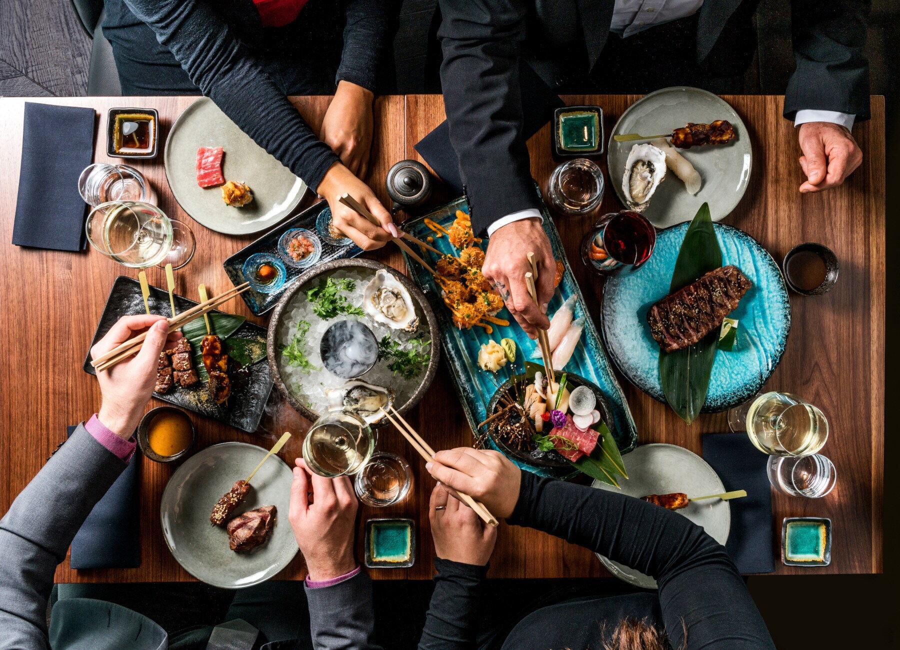 Hände nehmen mit Stäbchen Essen von Tellern in der Mitte eines Tisches