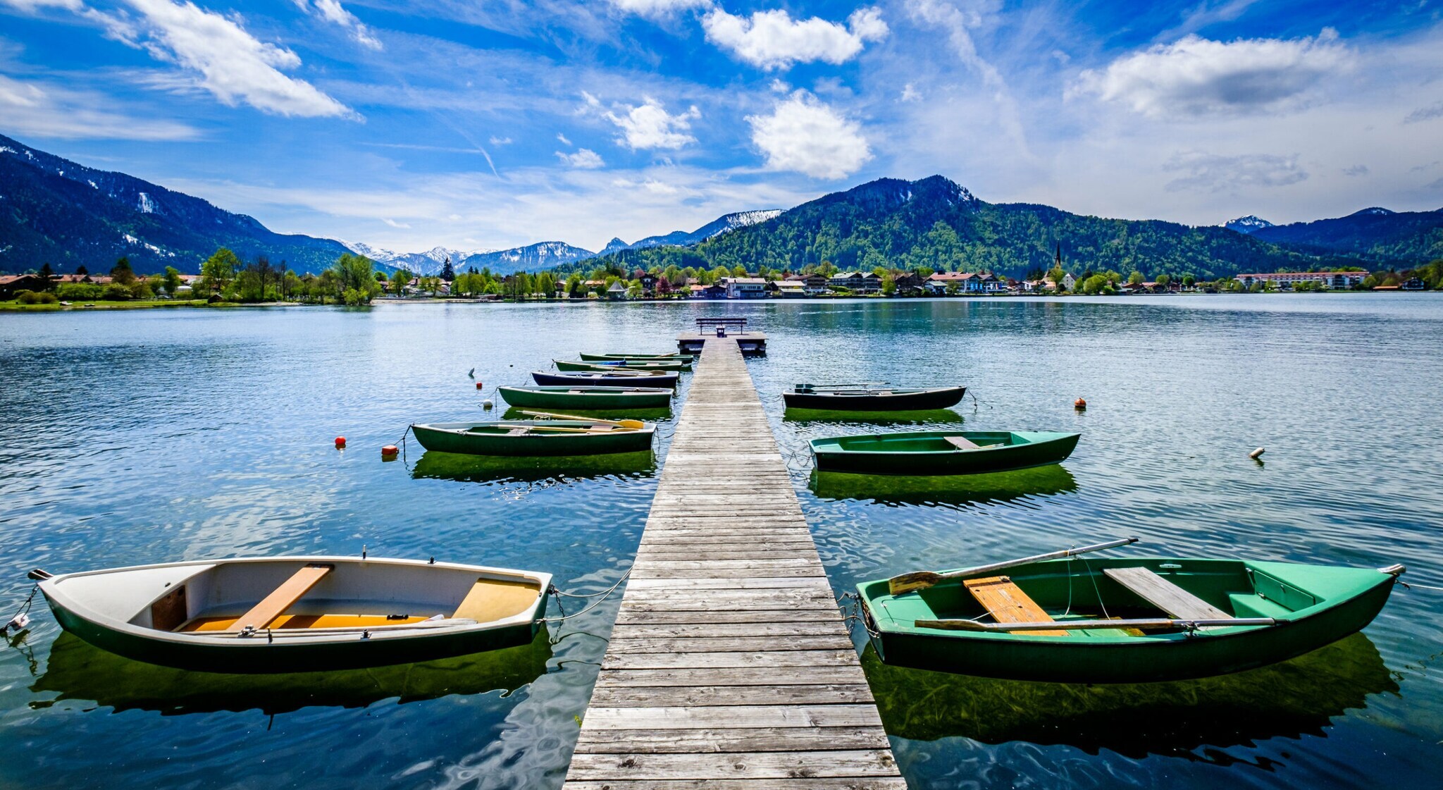 Ein Holzsteg mit kleinen Booten auf einem See, im Hintergrund Berge