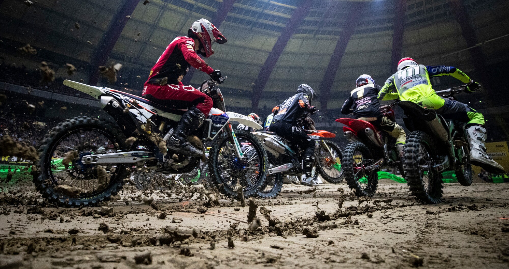 Mehrere Personen fahren mit ihrem Motocross in einer Halle neben- und hintereinander Mehrere Personen fahren mit ihrem Motocross in einer Halle neben- und hintereinander