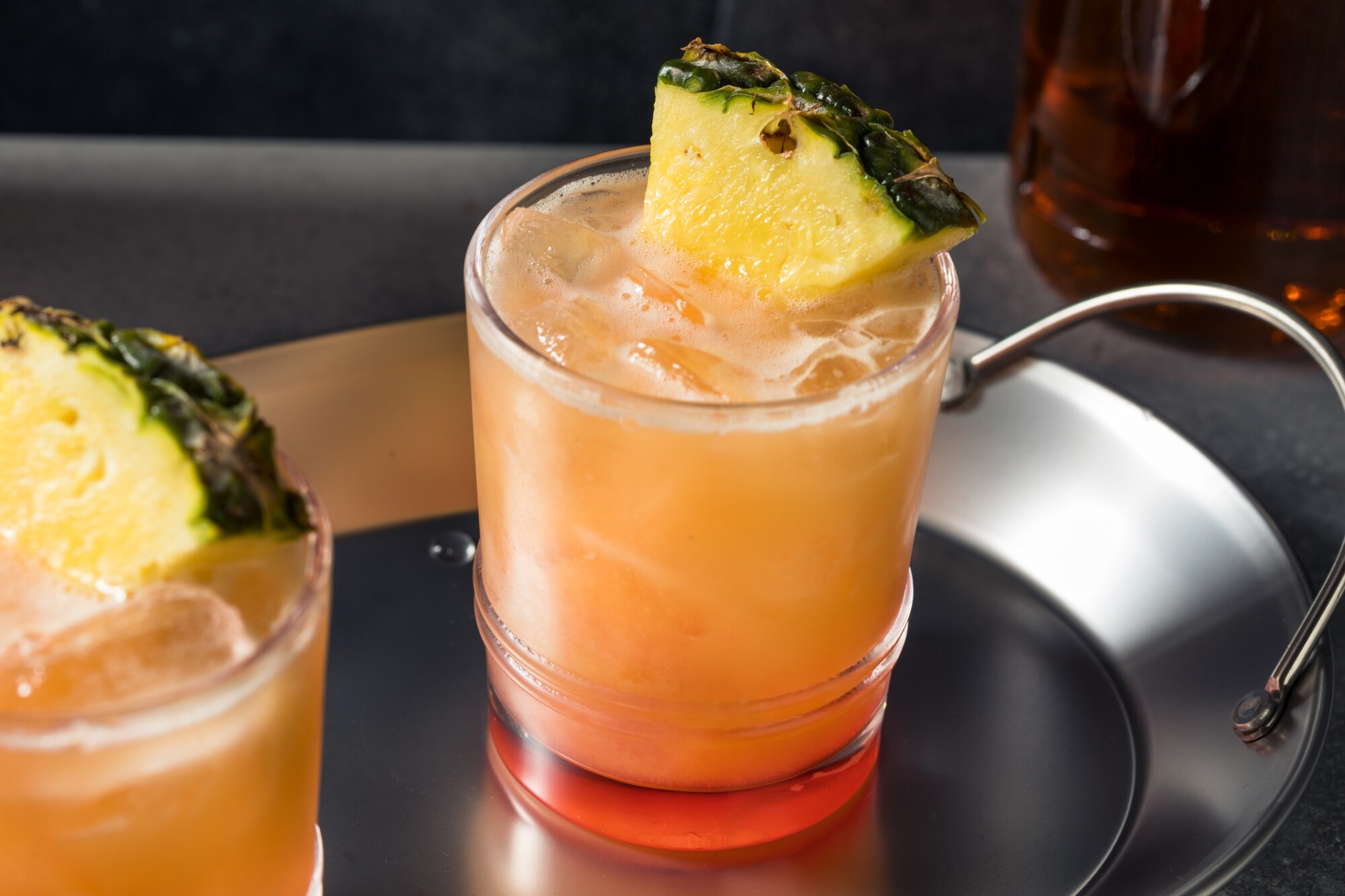 Zwei Gläser auf einem Silbertablett mit orangefarbener Flüssigkeit und einer Ananasscheibe als Dekoration