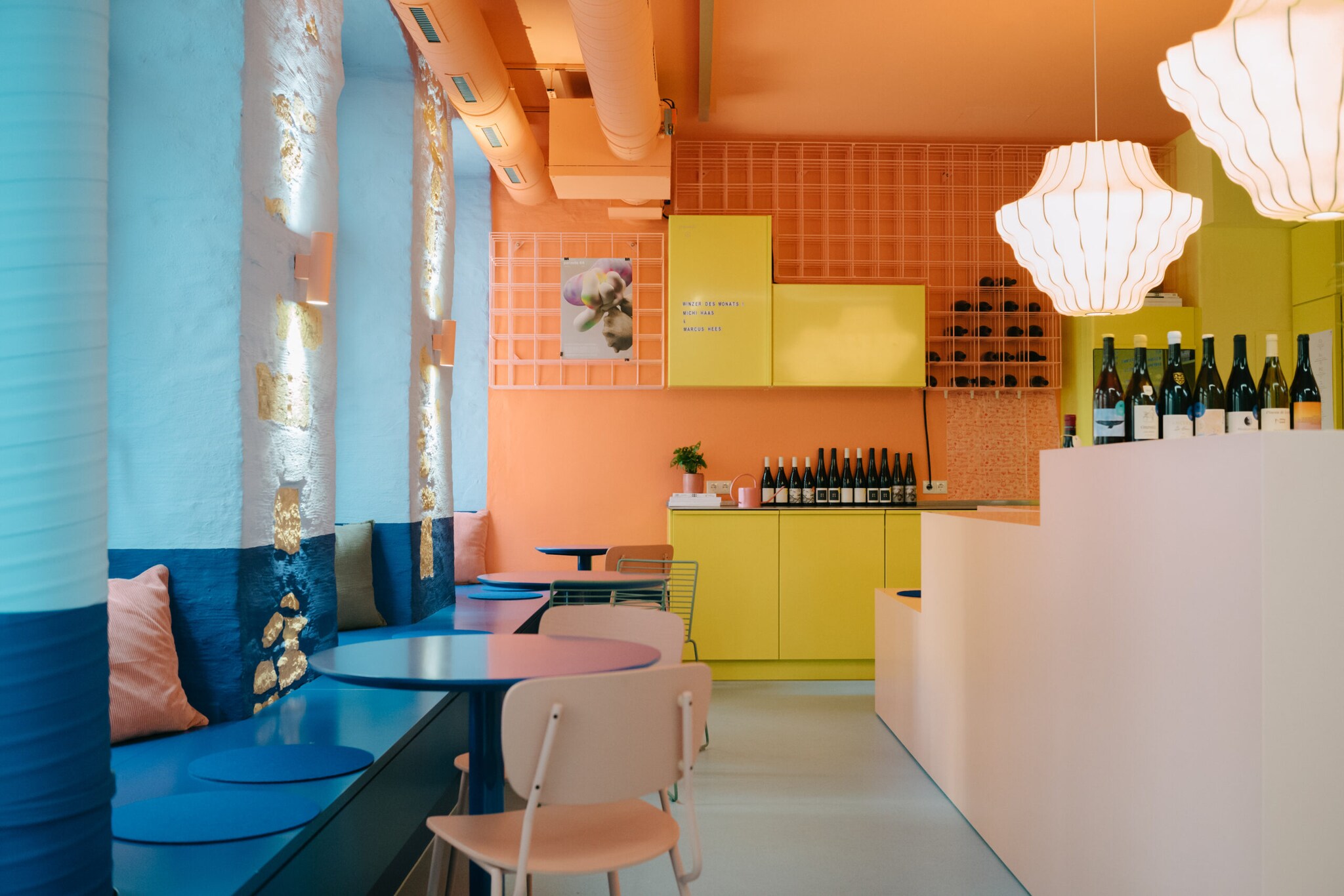 Der moderne Sitzbereich im Tipsy mit blauen Tischen, rosa Stühlen und Tresen vor einer orangenen Fliesenwand
