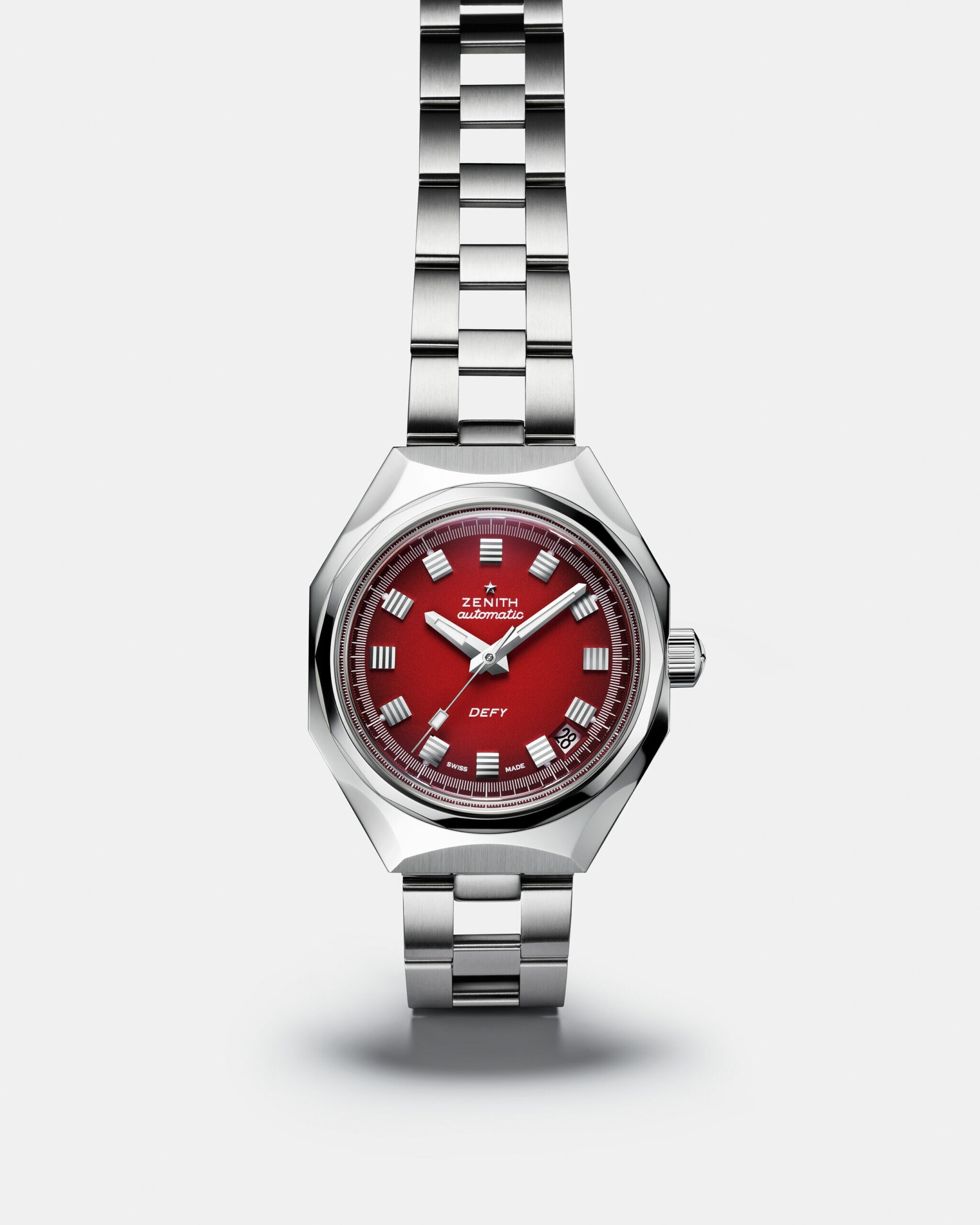 Silberne Armbanduhr mit rotem Ziffernblatt auf einem grünen Kissen Silberne Armbanduhr mit rotem Ziffernblatt auf einem grünen Kissen