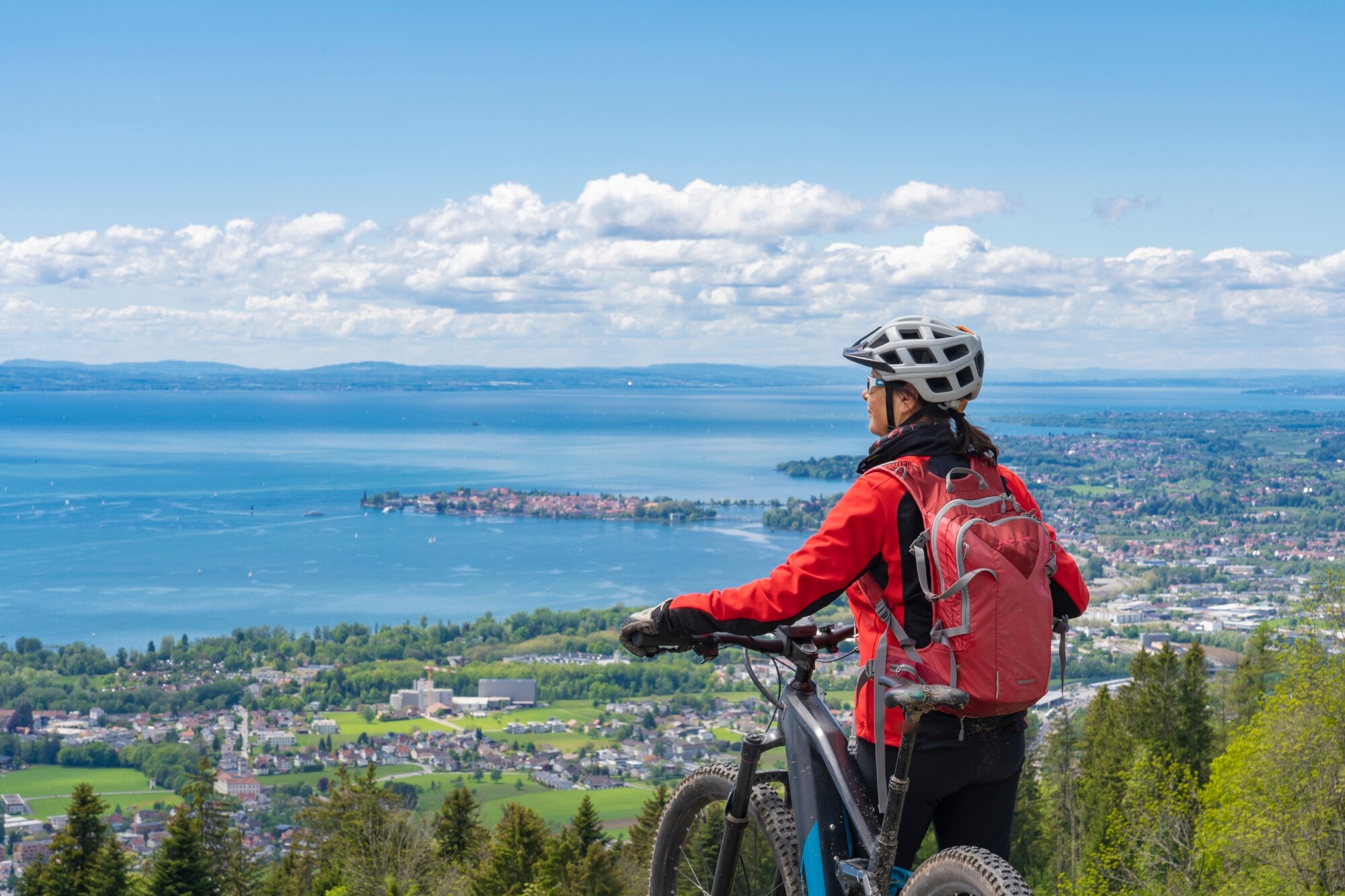 Rückansicht einer Frau mit einem Fahrrad vor dem Panorama des Bodensees Rückansicht einer Frau mit einem Fahrrad vor dem Panorama des Bodensees