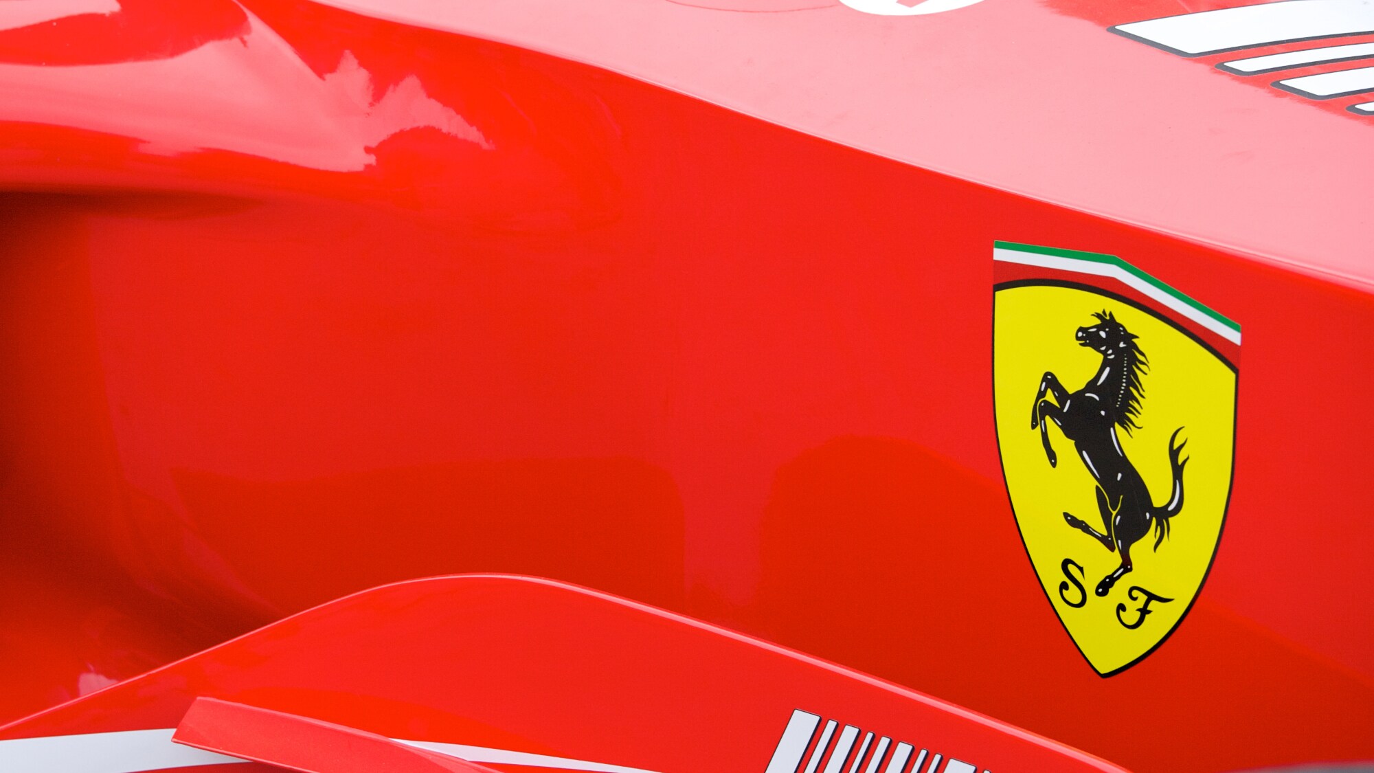 Detailaufnahme eines roten Rennwagens des Herstellers Ferrari mit dem Markenlogo eines sich aufbäumenden Pferdes in einem gelben Wappen