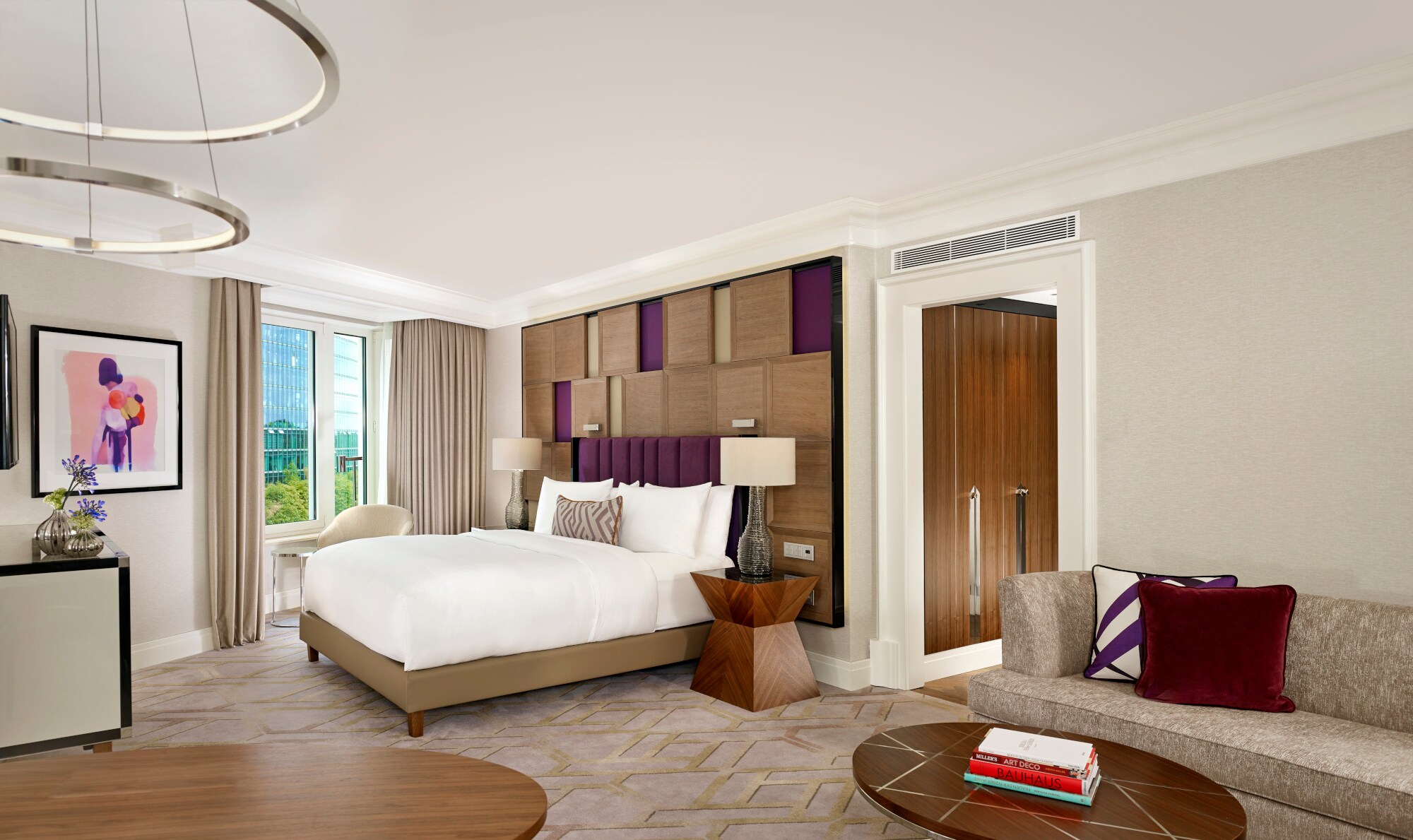 Ein Hotelzimmer mit Doppelbett, Tischen und Sofa auf Teppichboden Eine moderne, helle Hotelsuite mit Doppelbett und Designelementen.