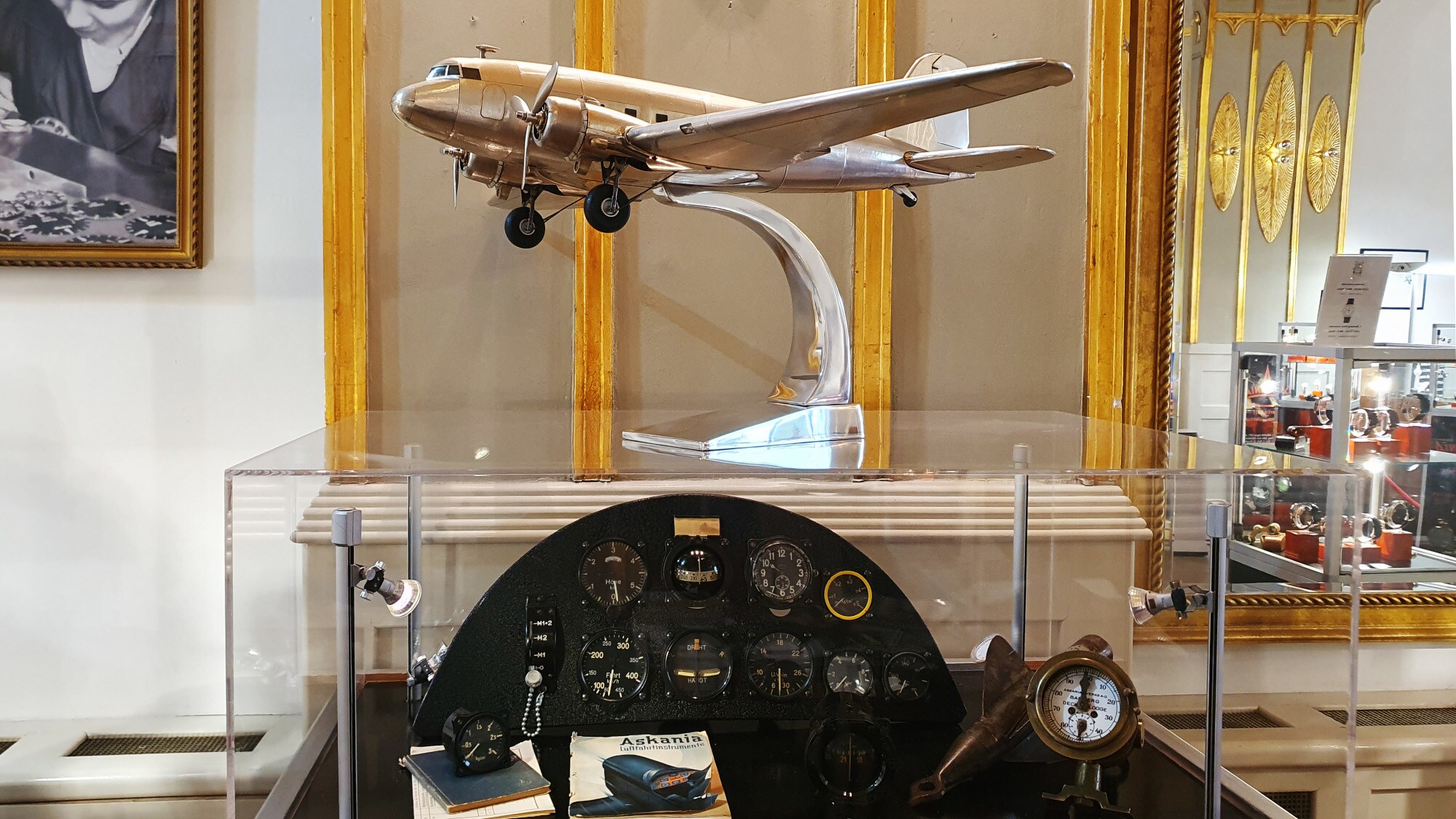 Glasvitrine mit antiken Bordinstrumenten, auf der sich ein metallisch glänzendes Flugzeugmodell befindet Glasvitrine mit antiken Bordinstrumenten, auf der sich ein metallisch glänzendes Flugzeugmodell befindet