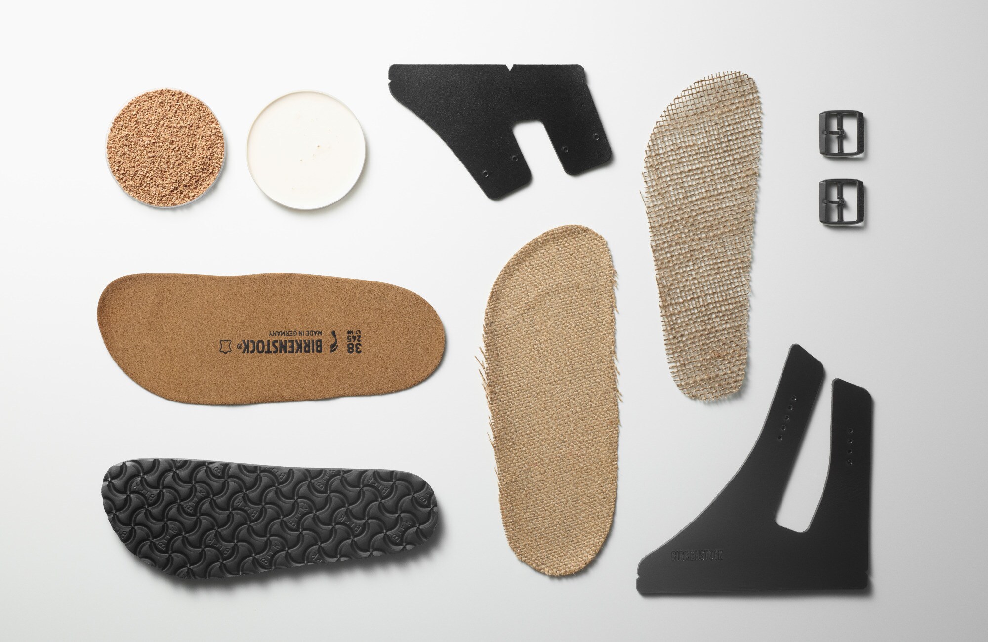 Aufsicht der Einzelteile einer Birkenstock-Sandale vom Fußbett bis zur Schnalle auf weißem Untergrund Aufsicht der Einzelteile einer Birkenstock-Sandale vom Fußbett bis zur Schnalle auf weißem Untergrund