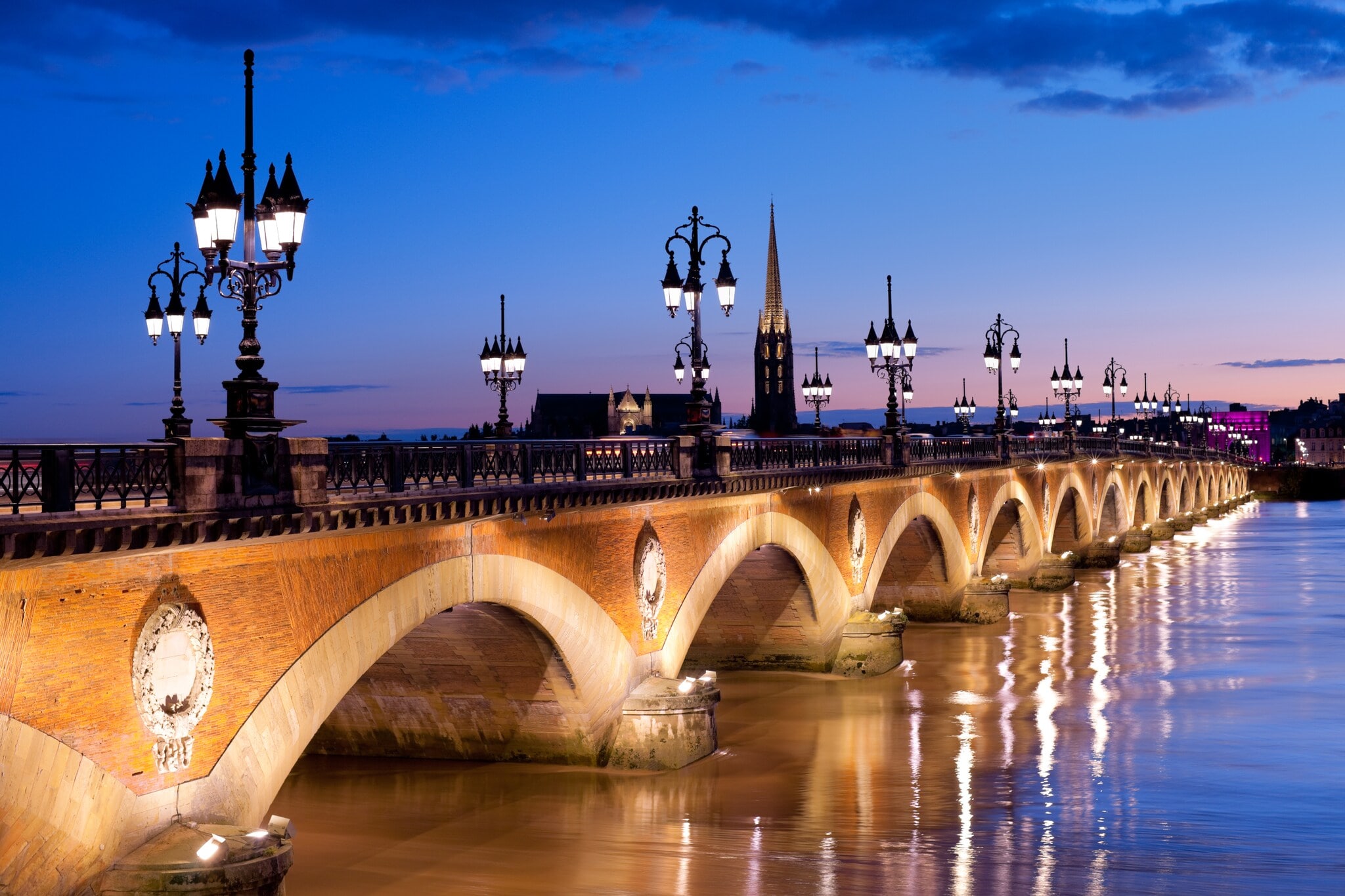 Eine alte Steinbrücke mit erleuchteten Straßenlaternen verläuft über einen Fluss in Bordeaux bei Nacht Eine alte Steinbrücke mit erleuchteten Straßenlaternen verläuft über einen Fluss in Bordeaux bei Nacht