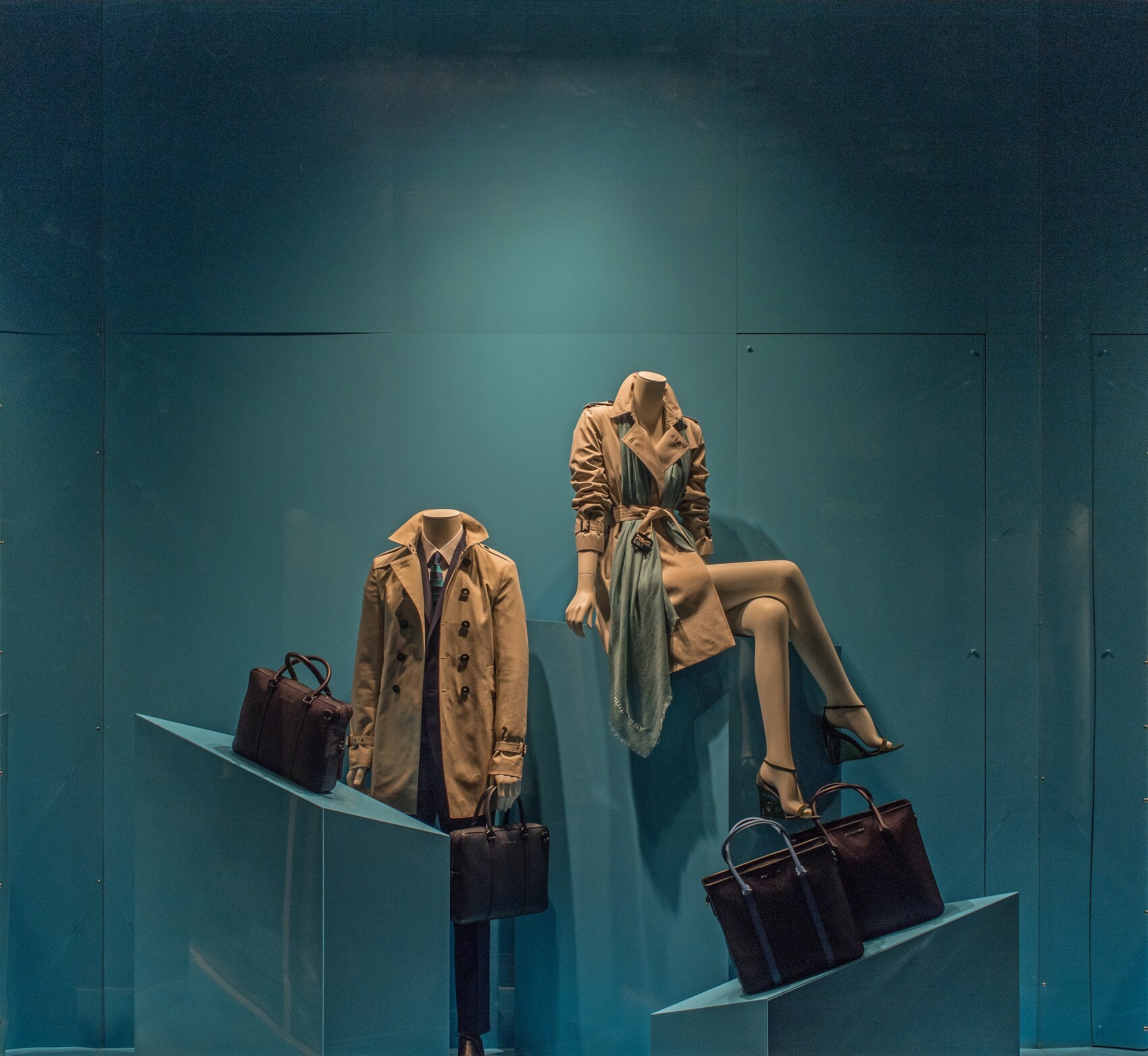 Ein brauner Damen- und an Herrenmantel an Schaufensterpuppen, davor Taschen auf Podesten Displays Ein brauner Damen- und an Herrenmantel an Schaufensterpuppen, davor Taschen auf Podesten