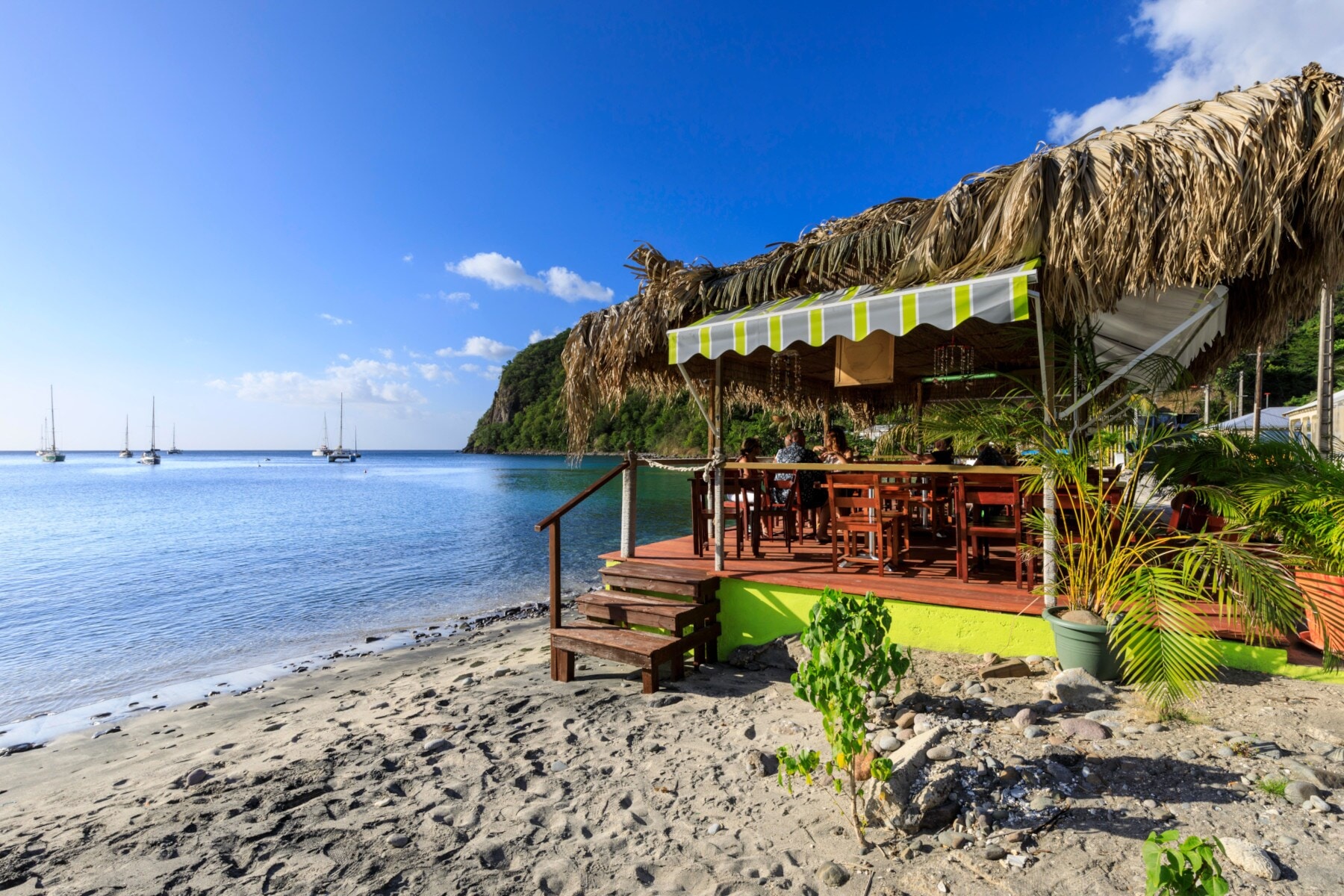 Eine Strandbar an einem Sandstrand in einer Bucht mit Segelbooten Eine Strandbar an einem Sandstrand in einer Bucht mit Segelbooten