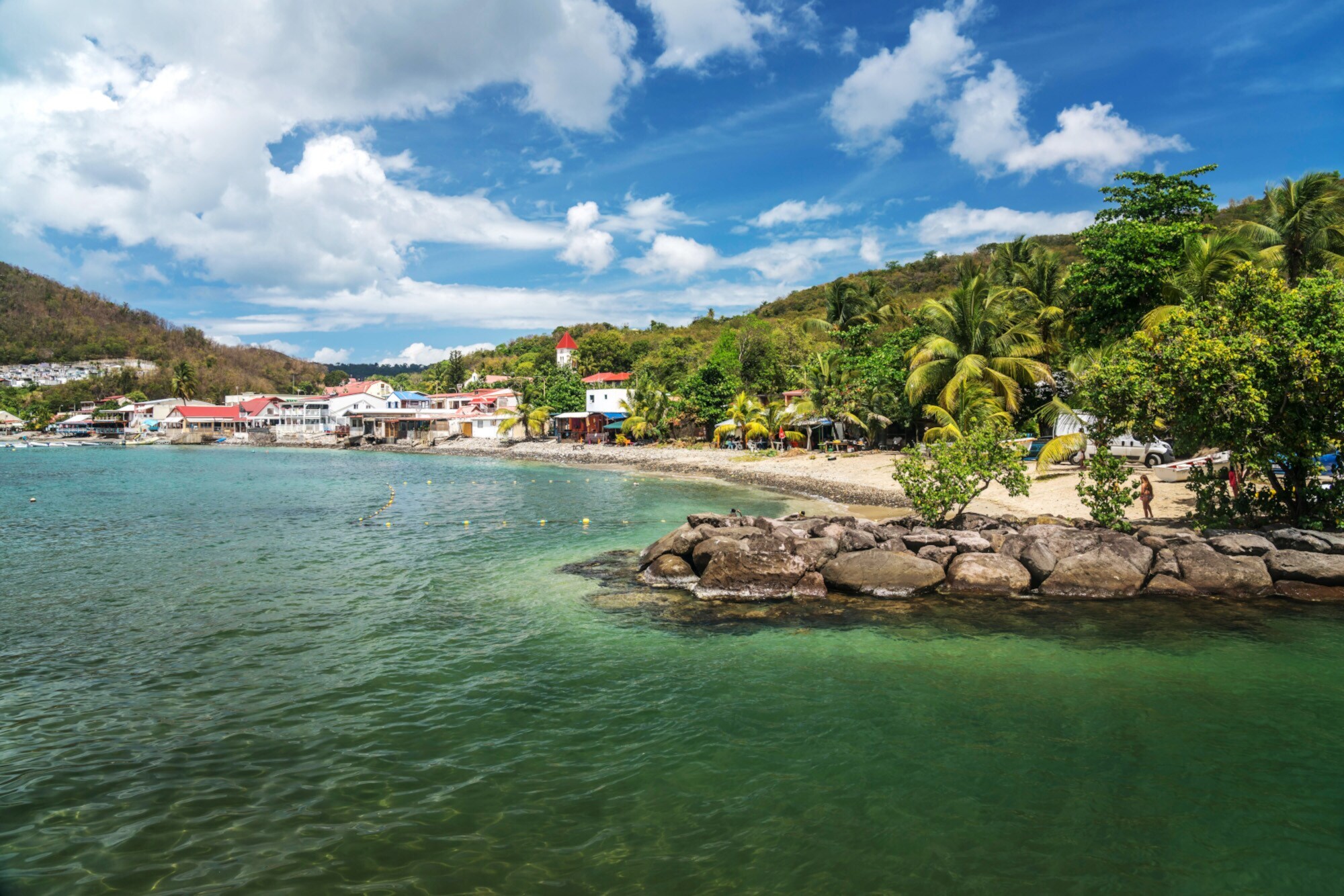 Ein kleines, karibisches Fischerdorf an einem Sandstrand in einer begrünten Bucht mit Palmen