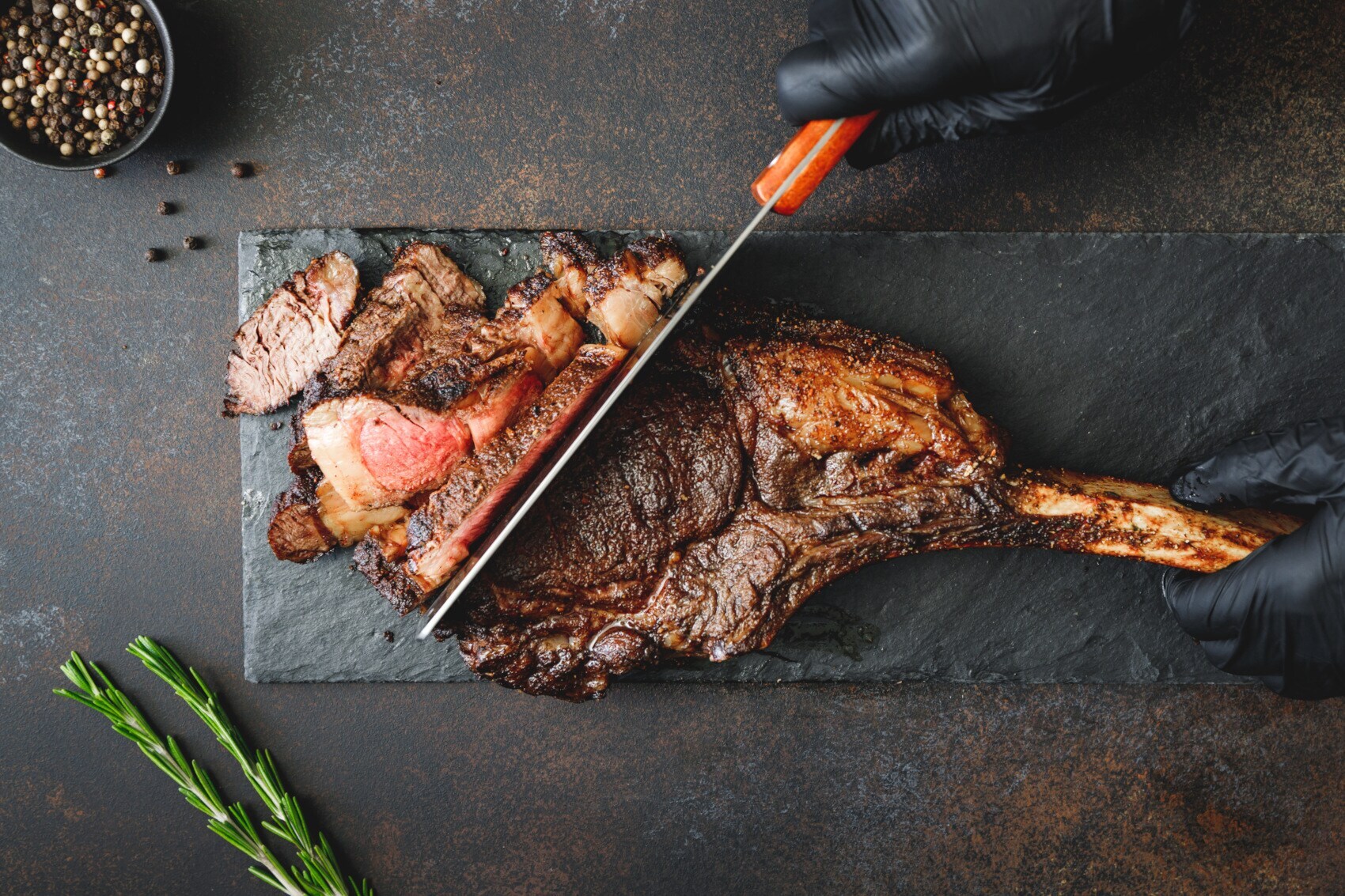 Topshot auf ein Stück Fleisch auf einer Schieferplatte, das gerade in Scheiben geschnitten wird