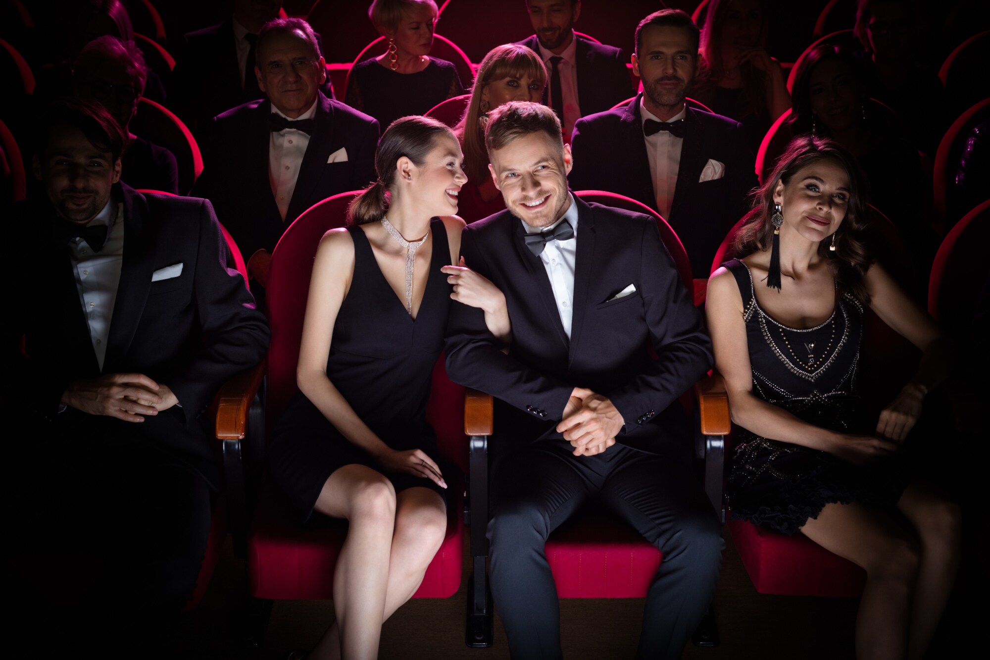 Mehrere schick gekleidete Menschen sitzen auf roten Stuhlreihen