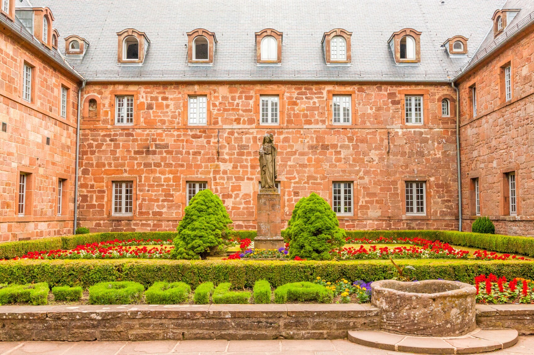 Blühender Klostergarten in einem Innenhof mit Sandsteinstatue in Frauengestalt im Zentrum